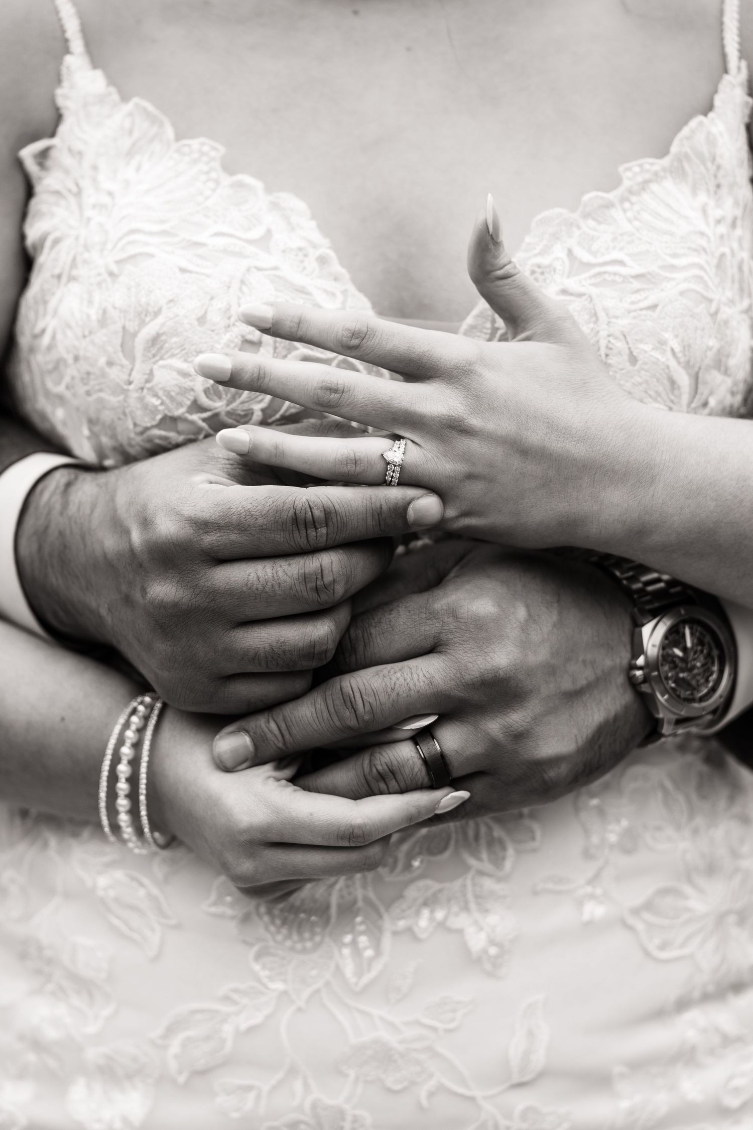 Artistic black and white detail of hands with wedding rings against lace dress.