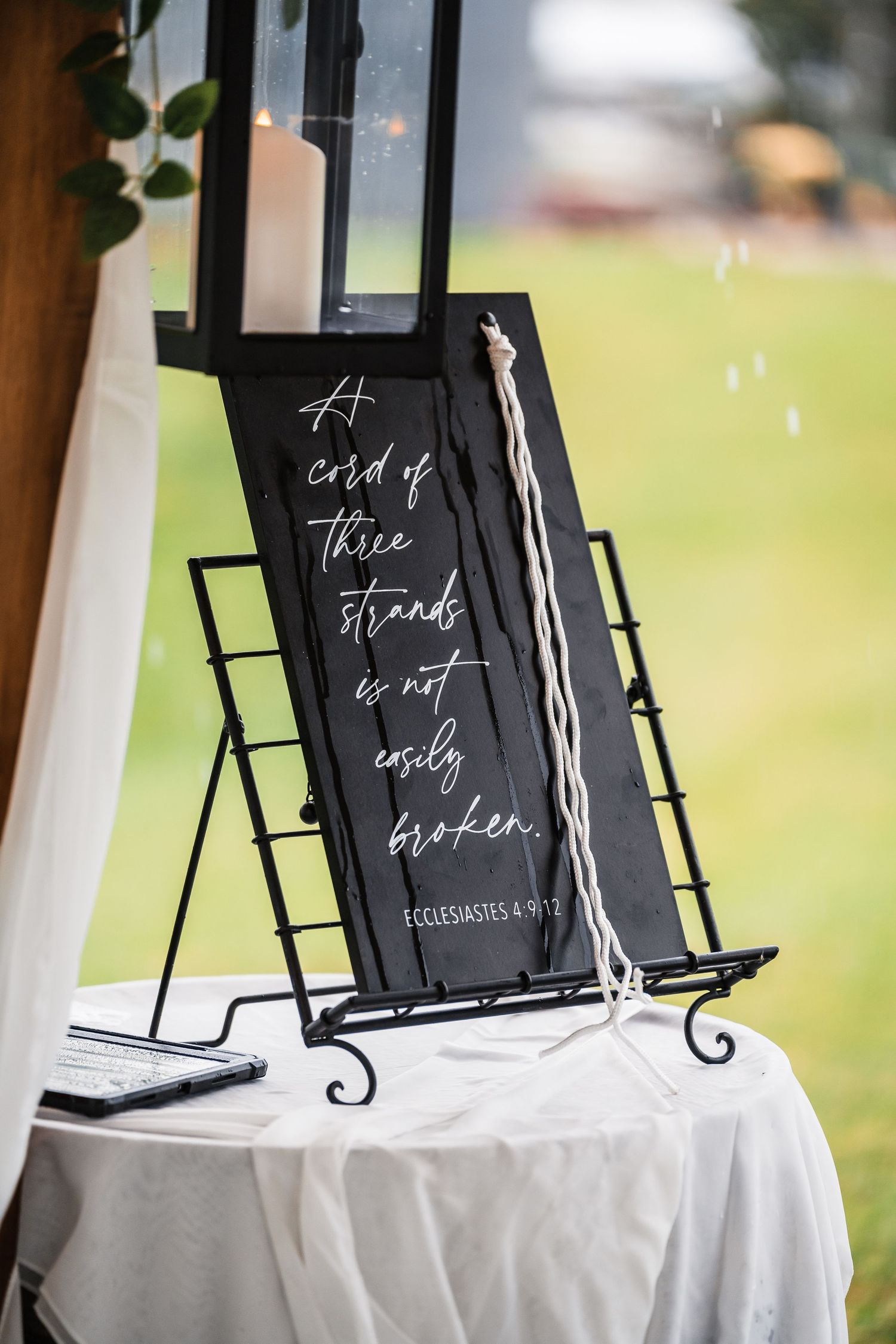 Black chalkboard signs with white calligraphy displayed on white tablecloths at an outdoor wedding reception.