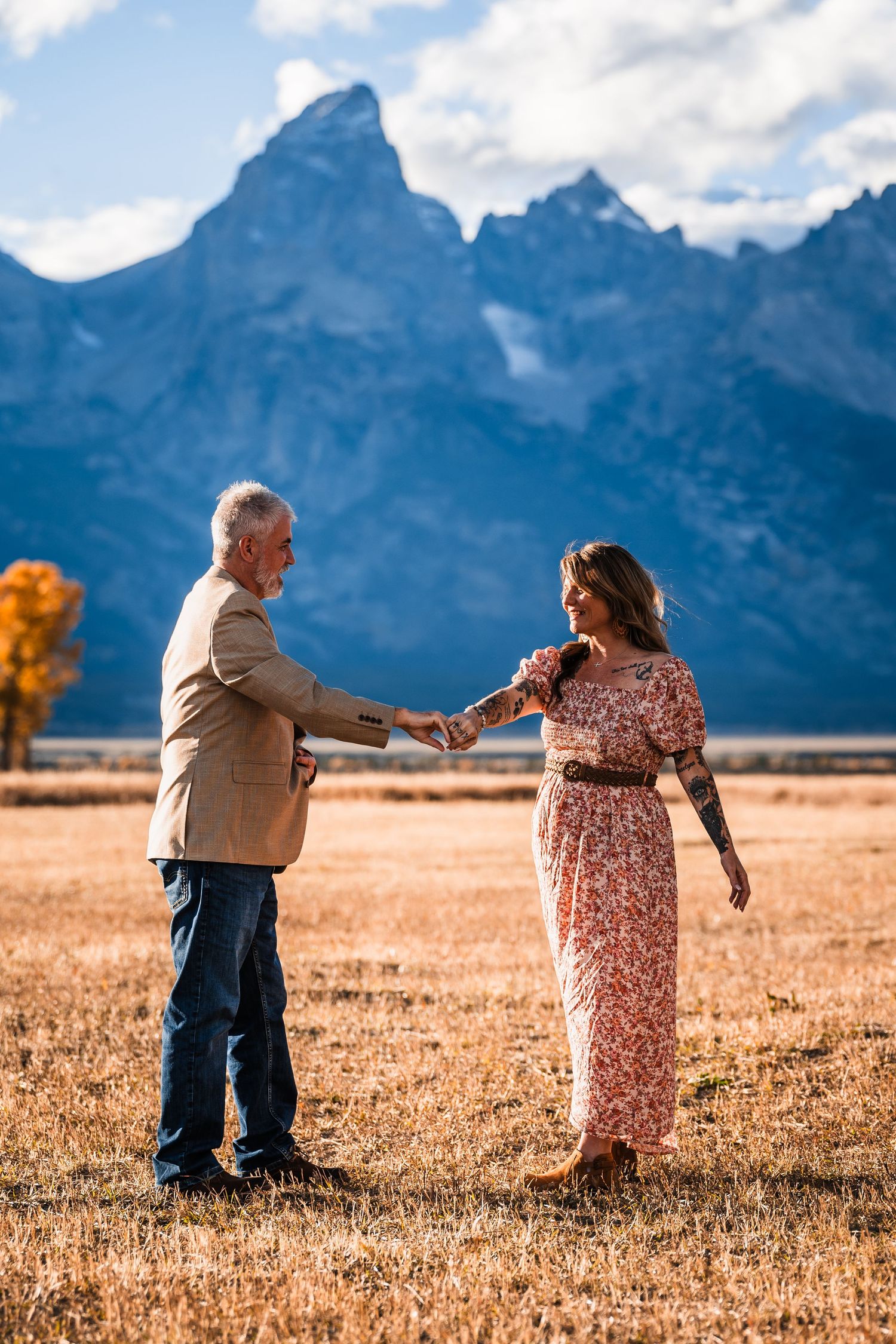 A couple dances together in a golden field with the majestic Grand Teton mountains rising dramatically in the background.