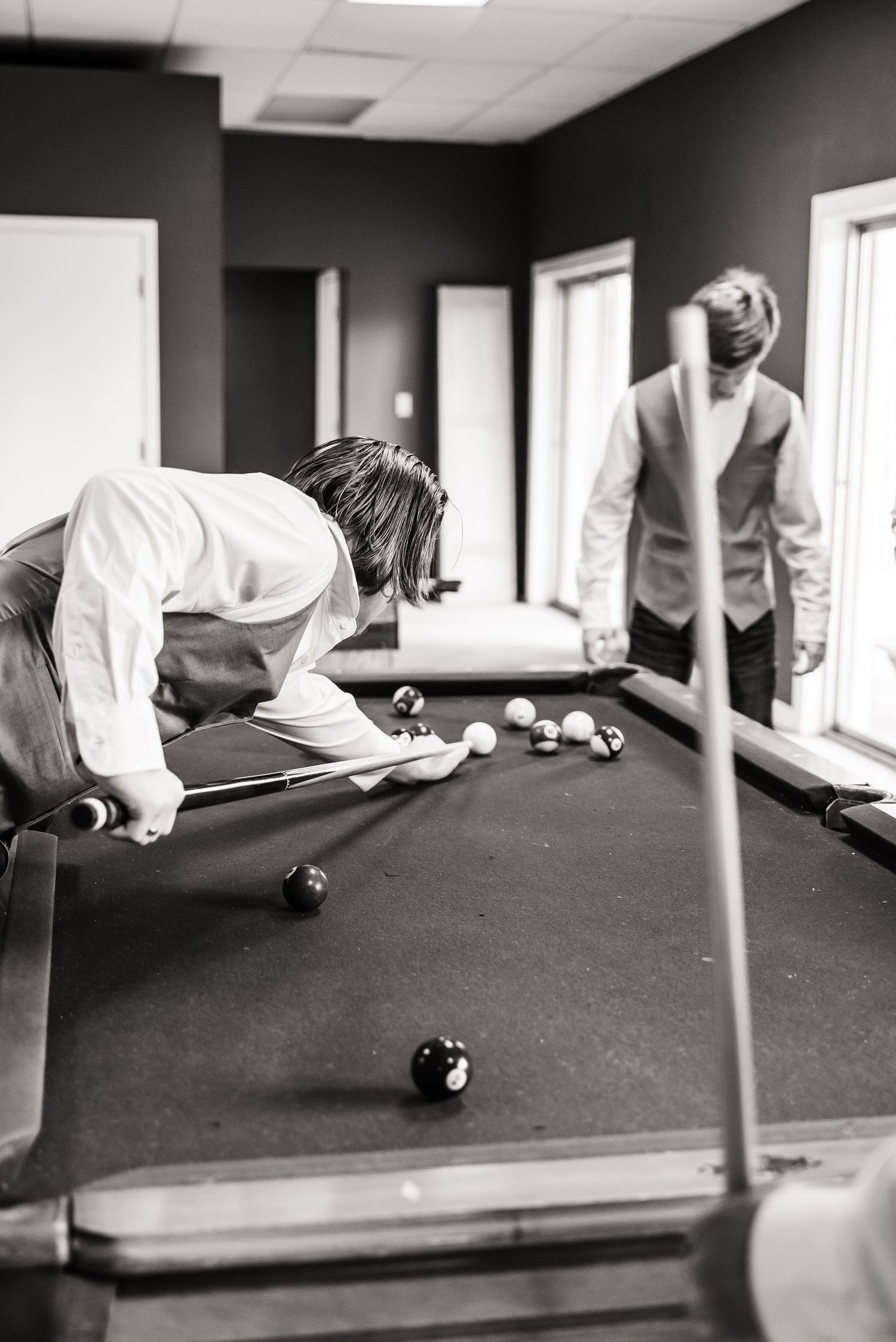 Two people playing pool in a dimly lit room during what appears to be a wedding celebration.