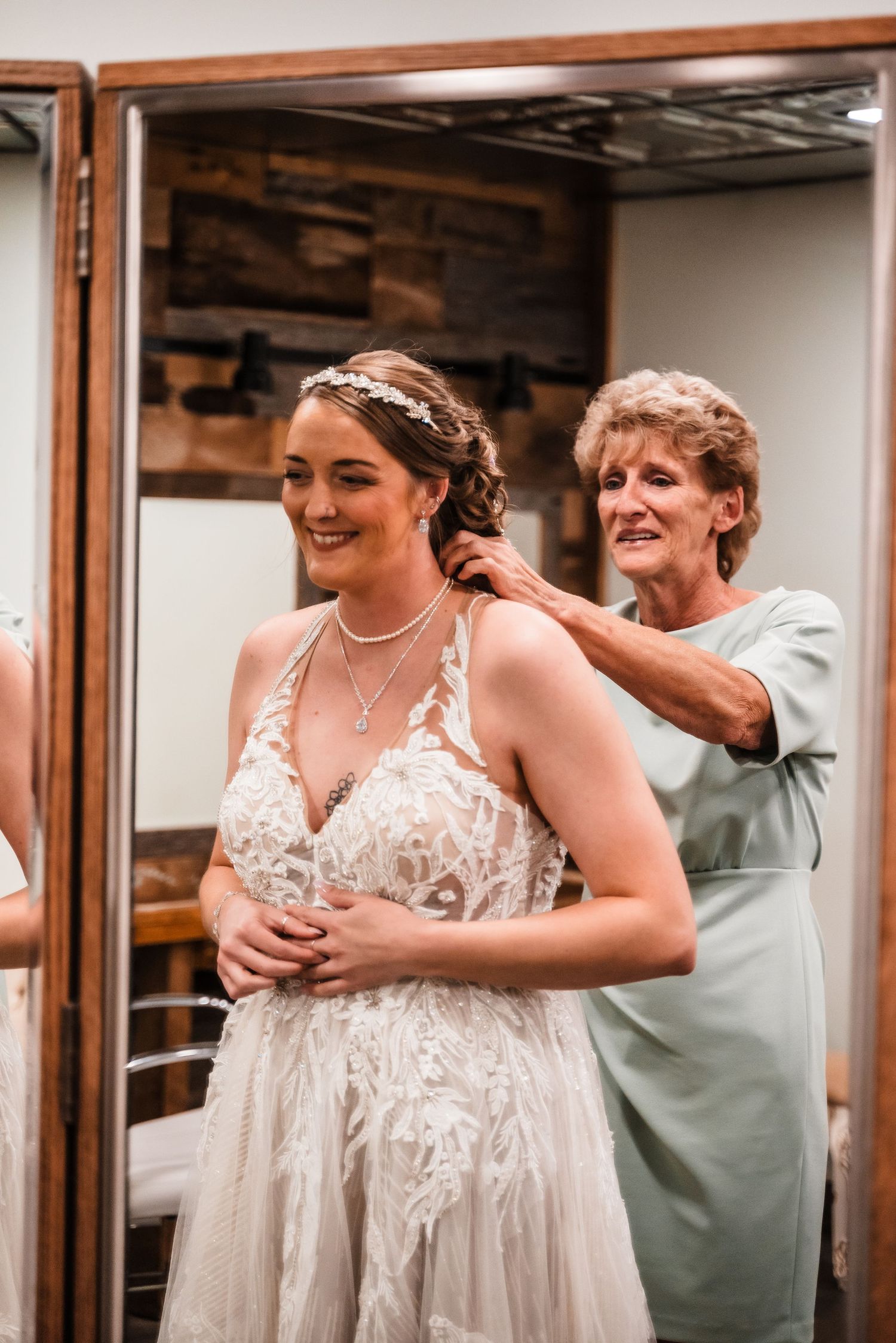 Getting ready scene of a bride in a lace gown having final dress adjustments made.