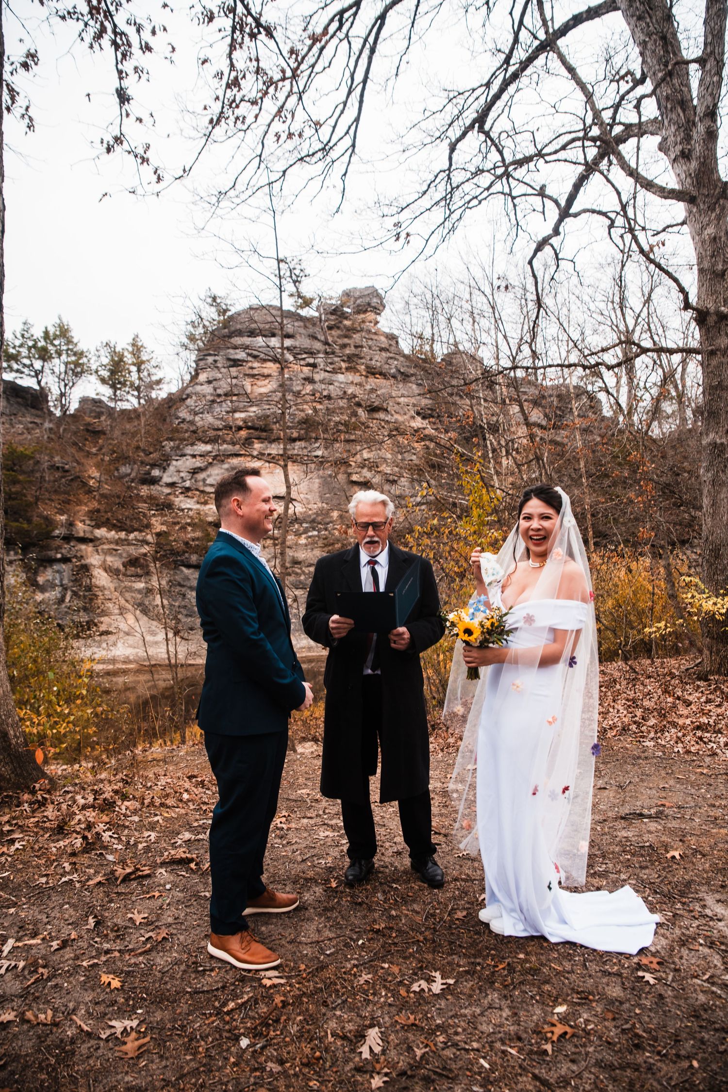 An outdoor wedding ceremony takes place in front of rocky cliffs during fall.