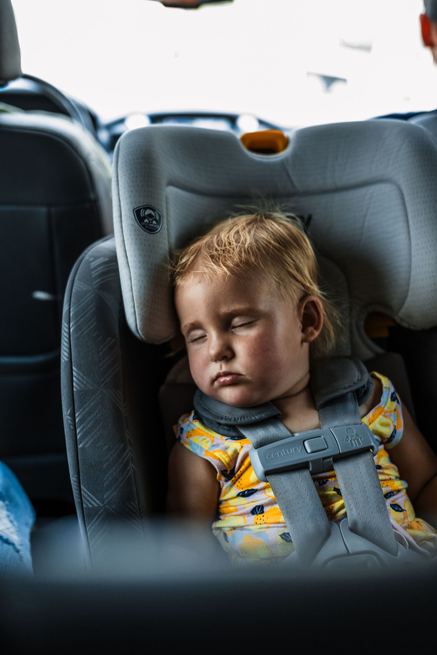 Young child sleeping peacefully in a gray car seat while traveling.