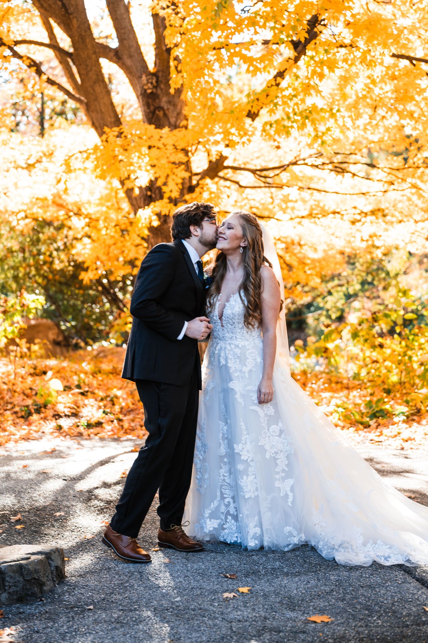 Newlyweds share intimate moment under golden autumn trees during wedding photoshoot.