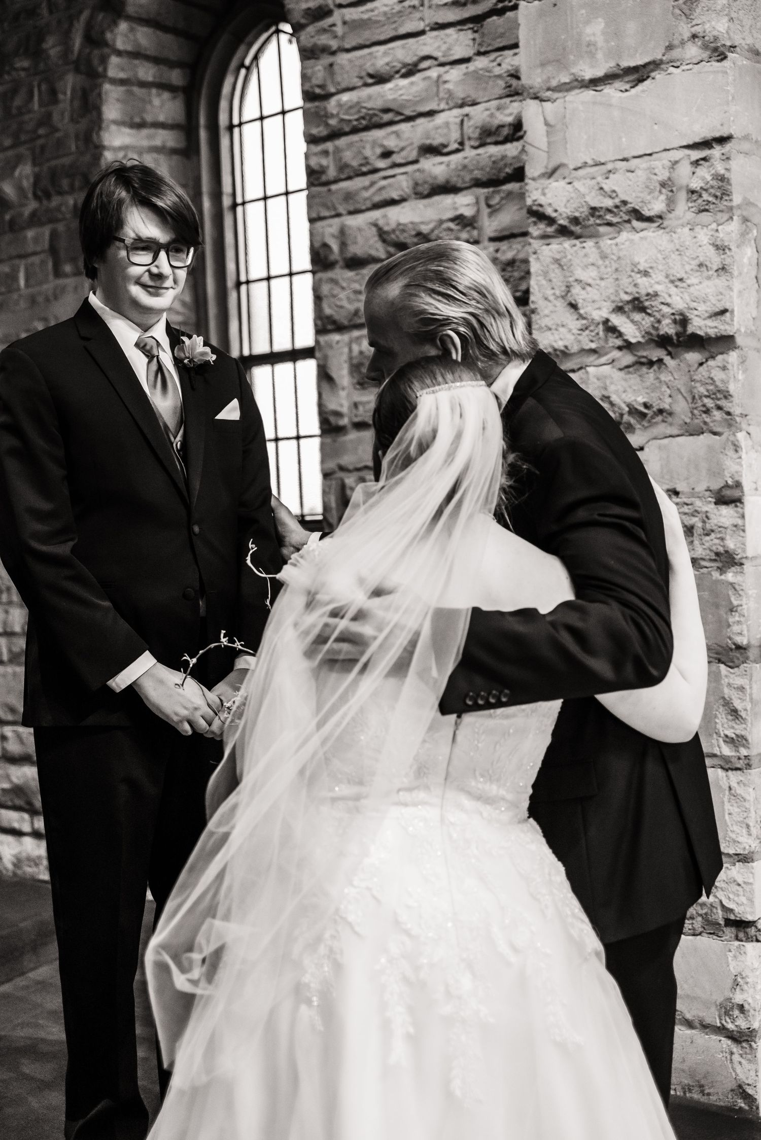 Black and white photo of wedding party adjusting bride's veil in stone church interior.