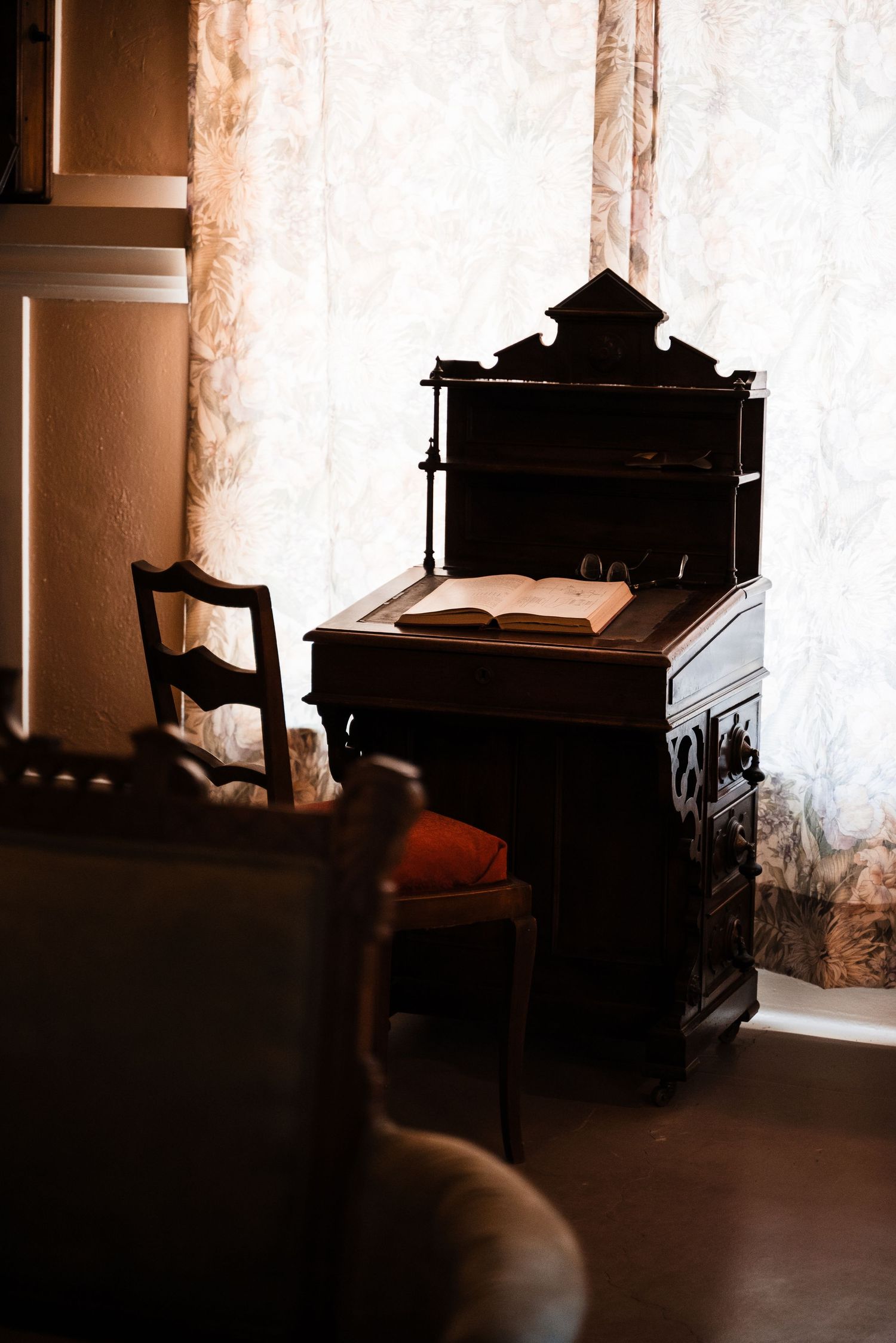 Antique wooden writing desk with an open book sits against a white wall in moody lighting.