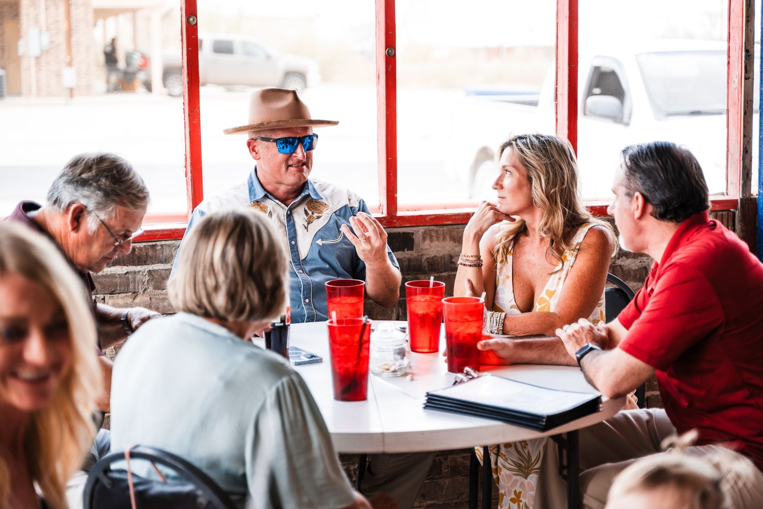 Group dining and socializing at casual restaurant with red cups and sunlit windows.