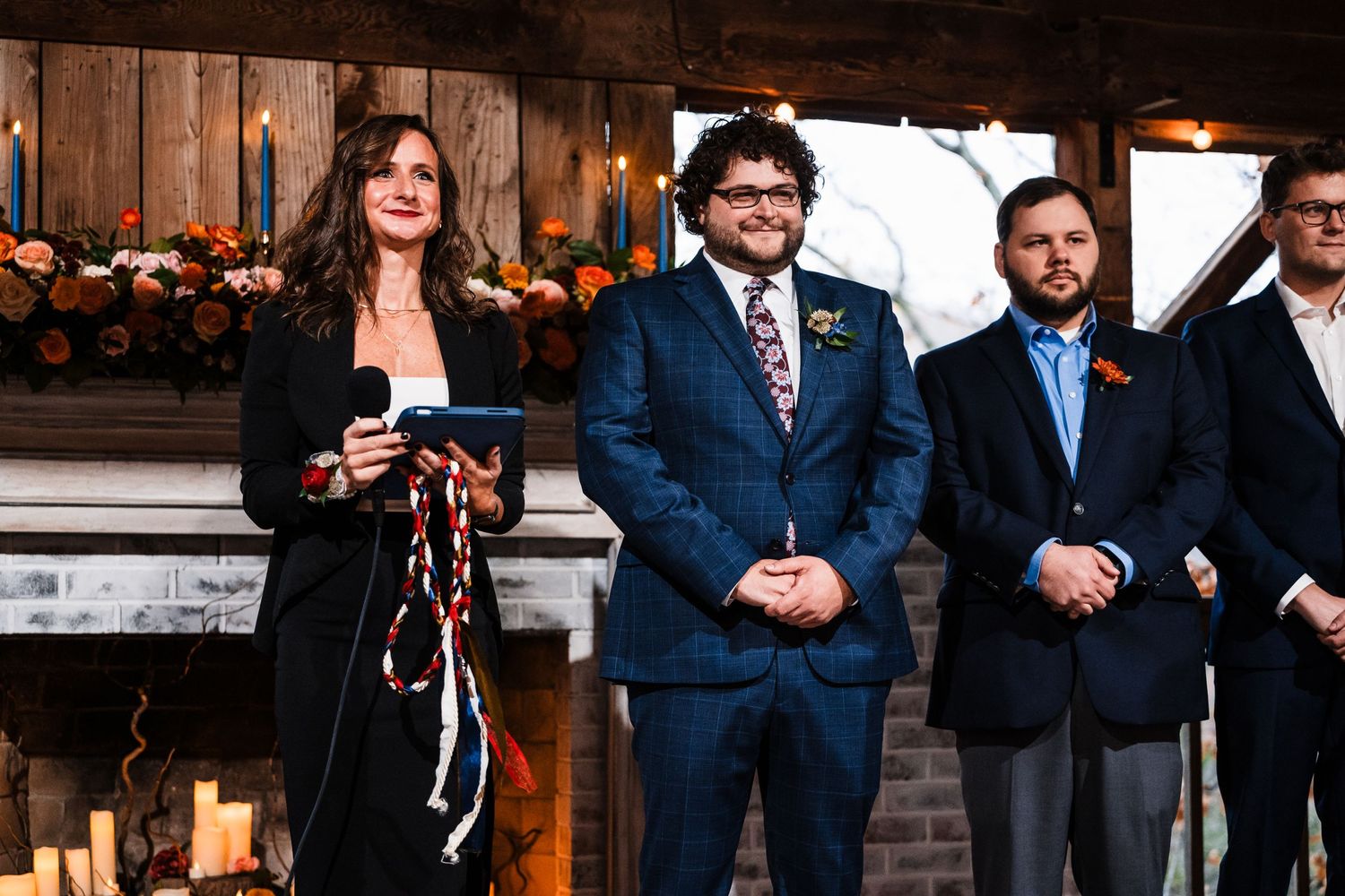 Wedding party members stand formally in front of a rustic wooden backdrop during ceremony.