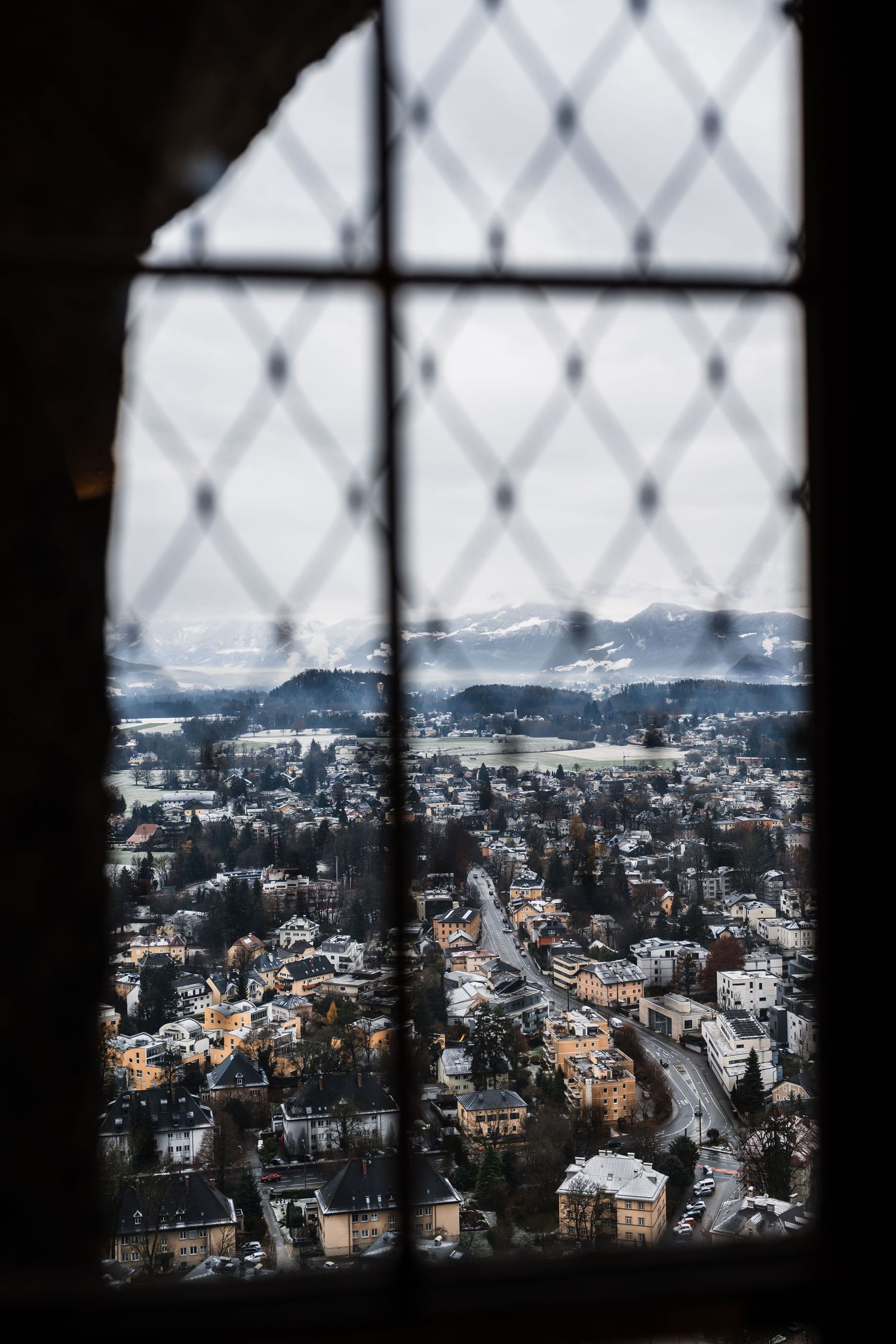 Snowy cityscape viewed through a diamond-patterned window with mountains in the background.