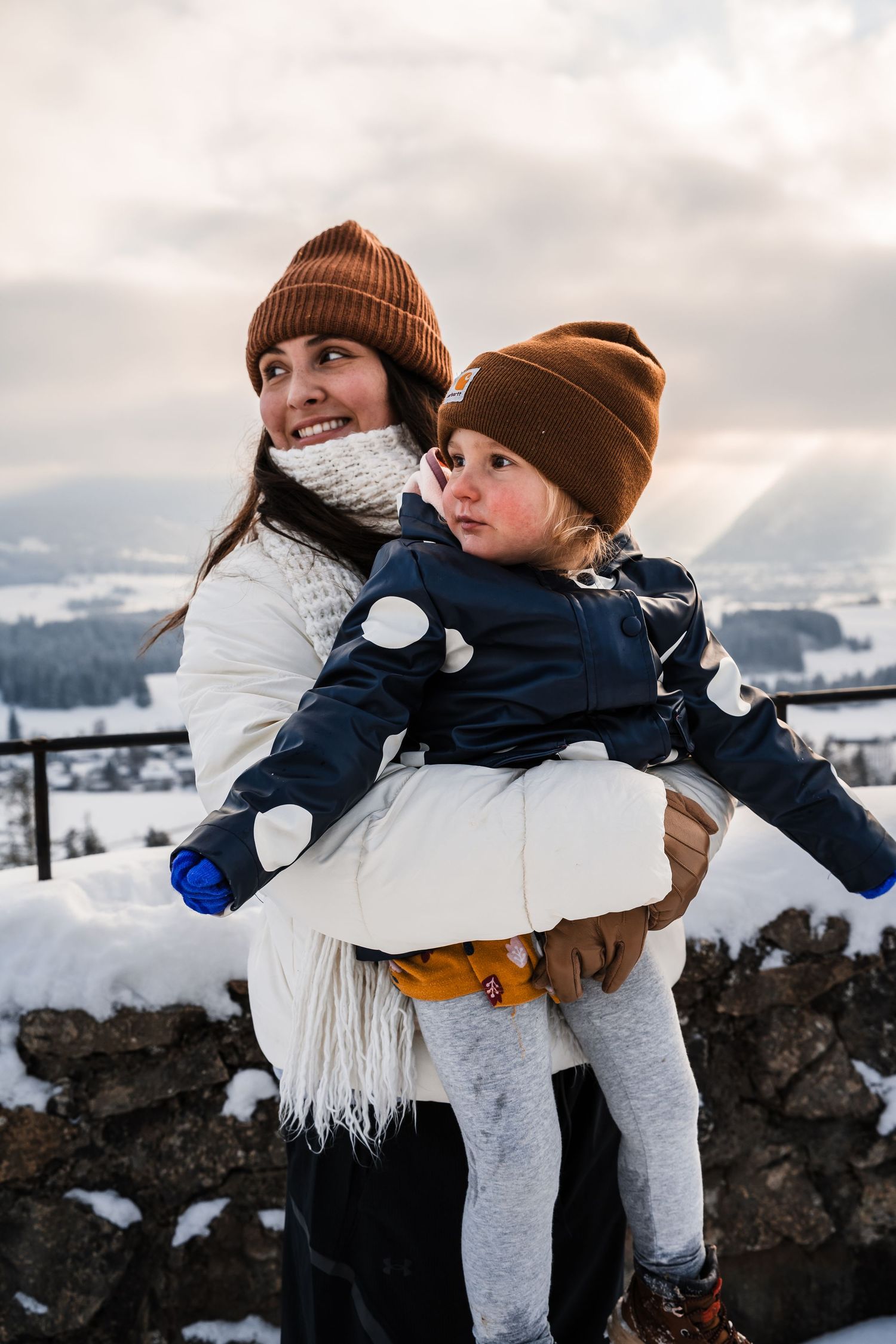 Two people in winter clothing and beanies share a joyful moment in the snowy mountains.