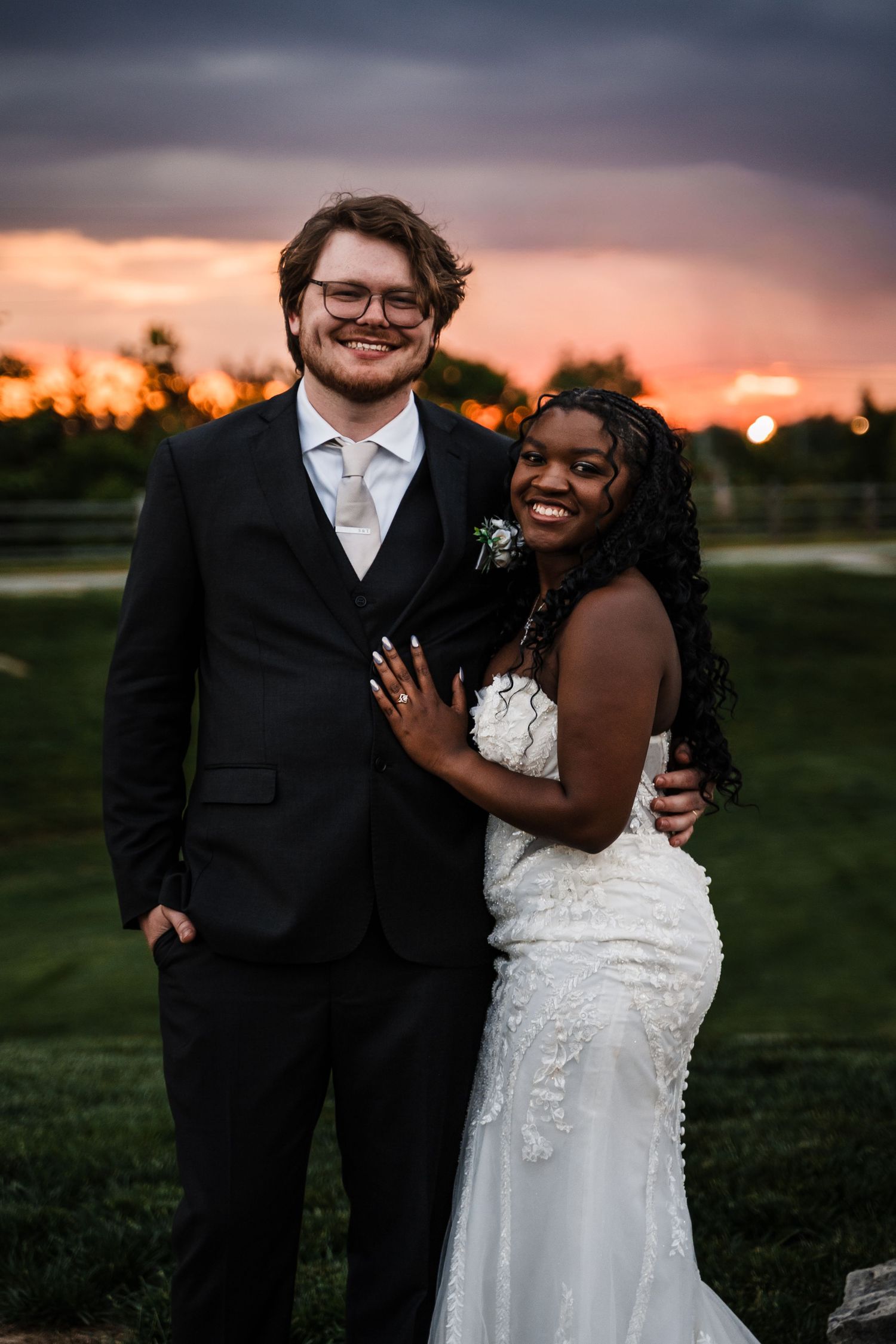 Bride and groom pose together smiling at sunset with vibrant orange sky in background.