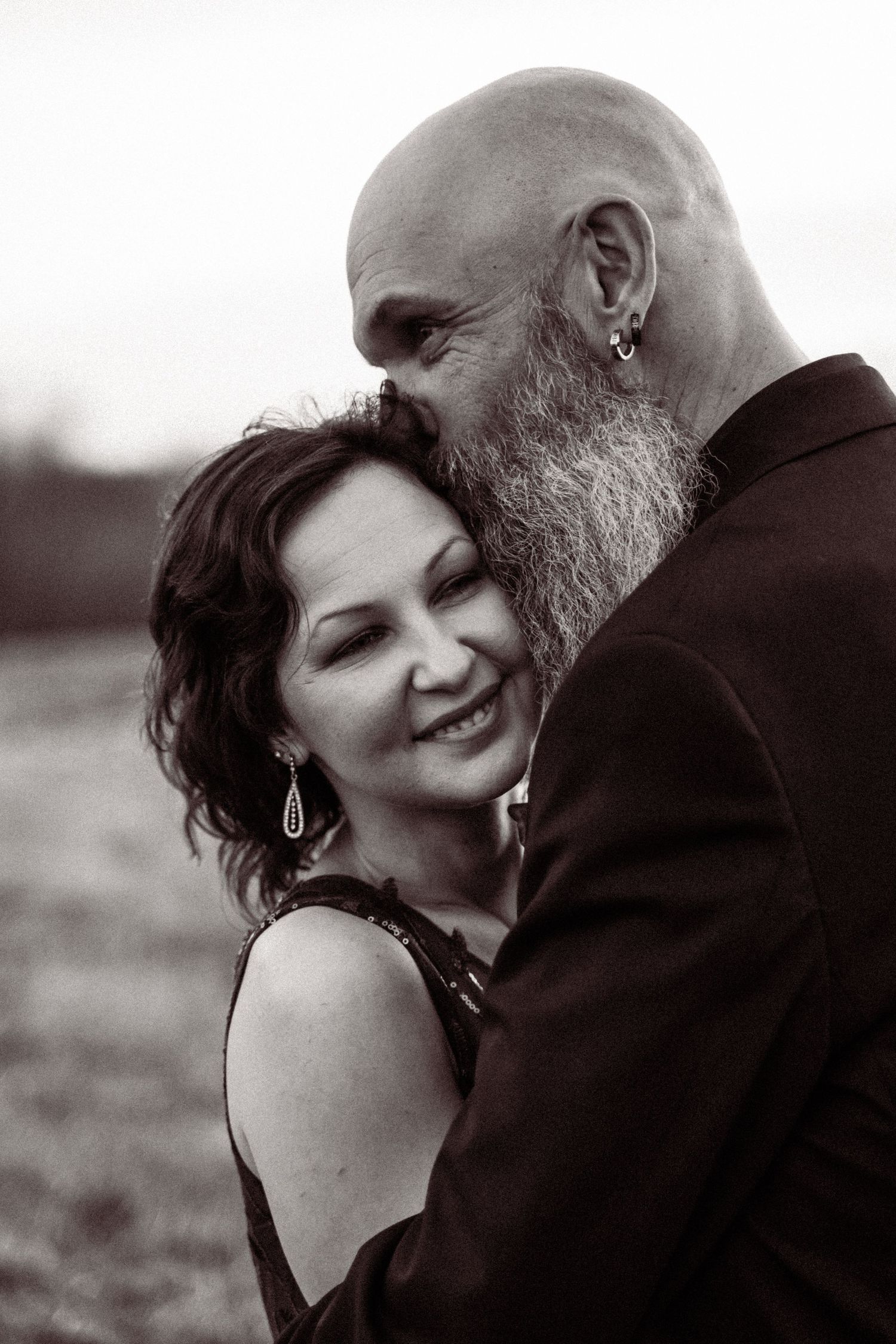Black and white portrait of smiling bride and bald bearded groom sharing a tender moment.