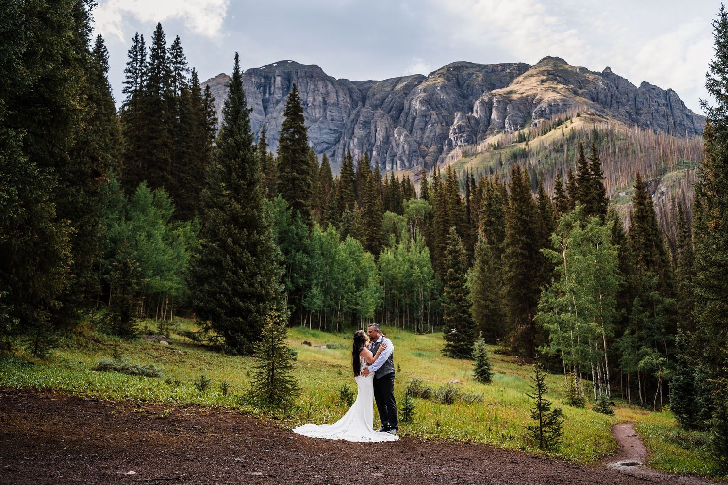 Bride and groom kissing in front of stunning mountain forest landscape with evergreen trees.