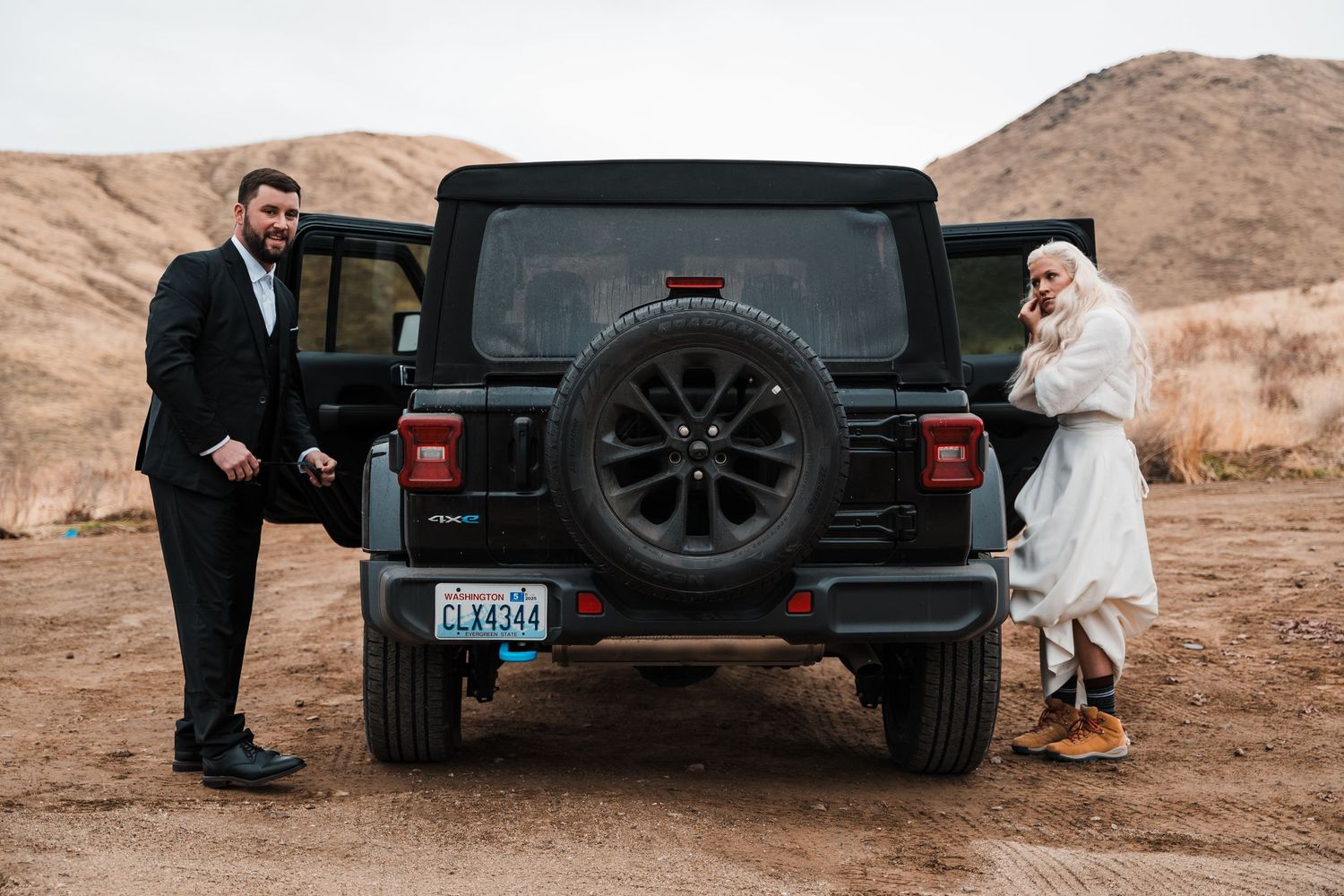 A black Jeep Gladiator parked in a desert landscape with people gathered around it during a photo session.