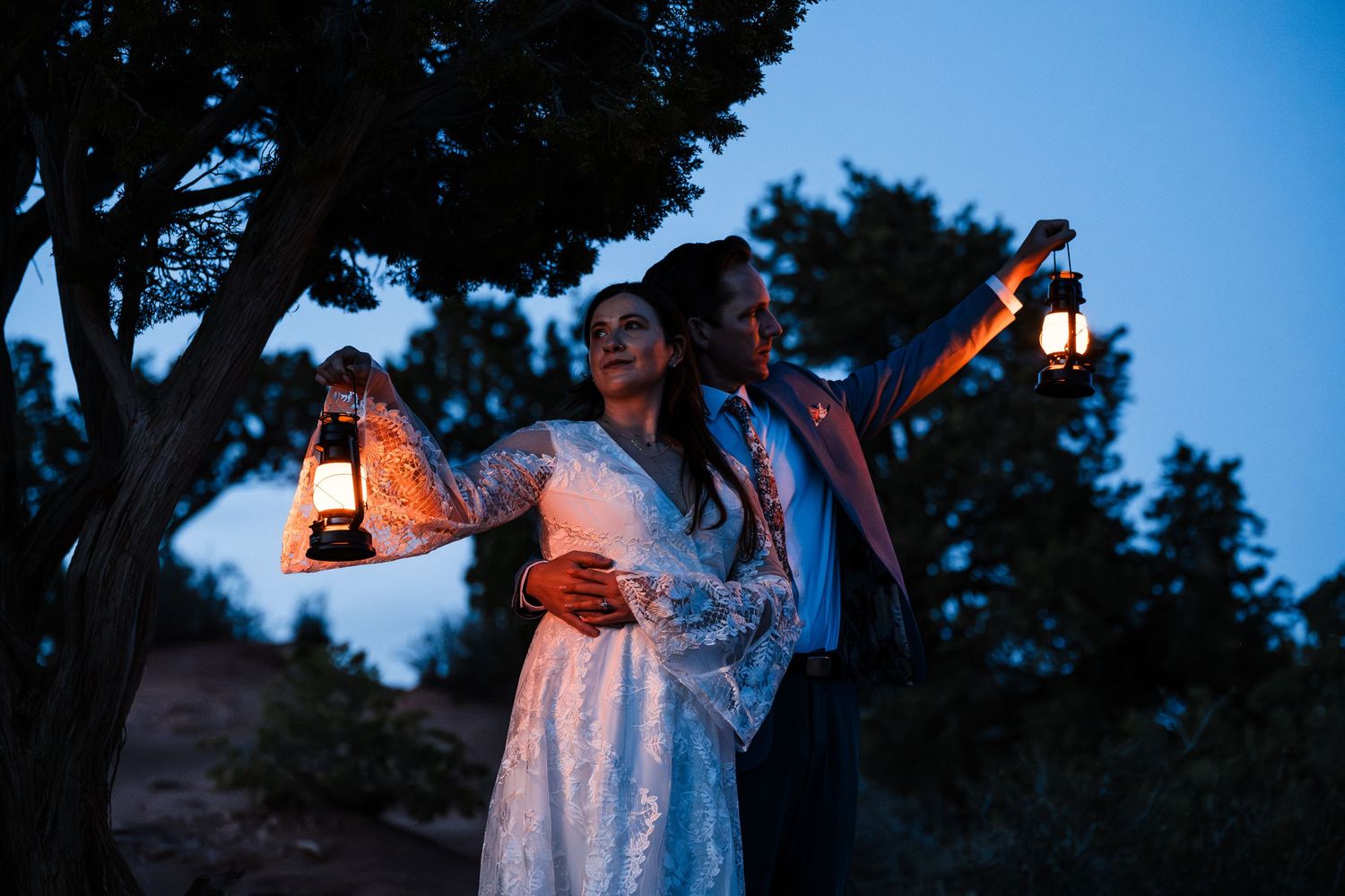Bride and groom holding vintage lanterns aloft in twilight blue outdoor wedding setting.