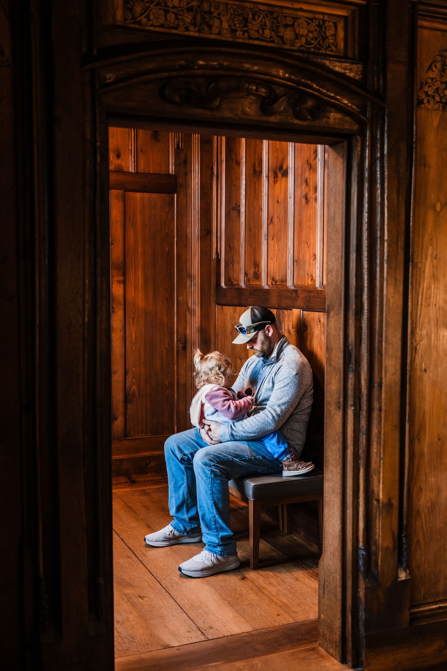 A series of wooden church pews shown in warm lighting with two people sitting together in one of the alcoves.