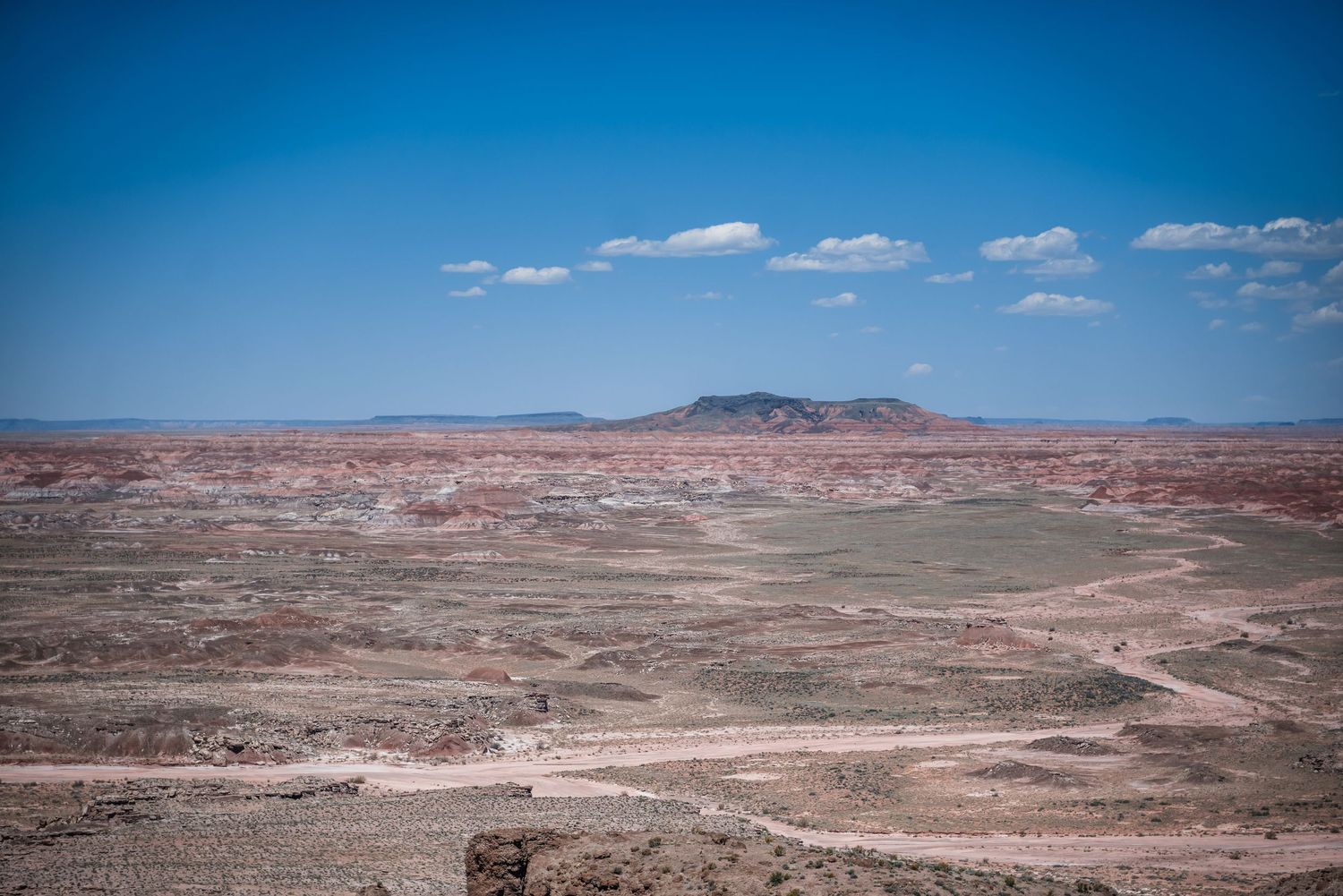Scenic desert landscape view of the Painted Desert in Arizona with layered red rocks under bright blue sky and white clouds.
