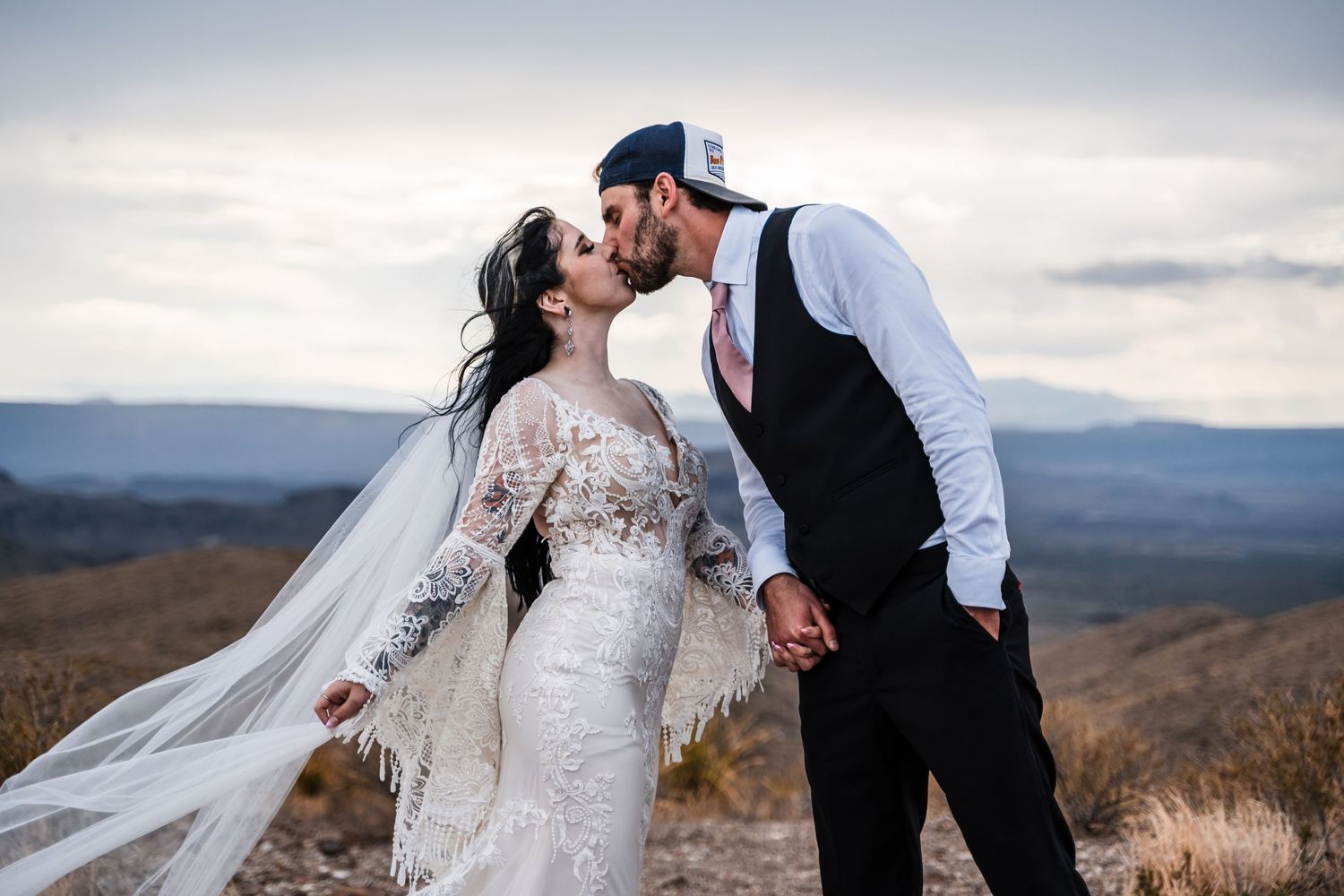 A romantic wedding moment captured against a backdrop of rolling mountains at sunset.