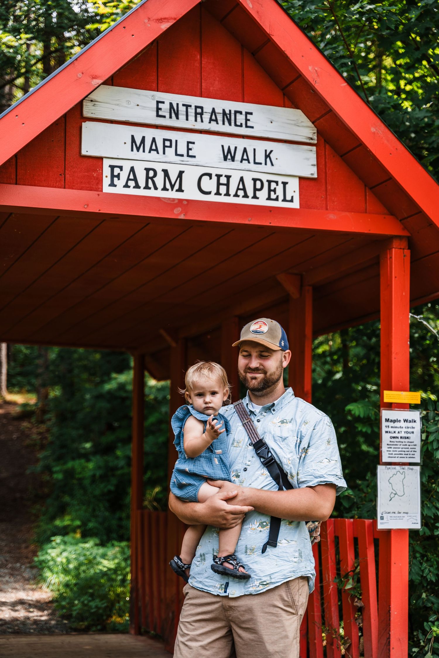 Red entrance sign for Maple Walk Farm Chapel with visitors standing beneath the wooden shelter.