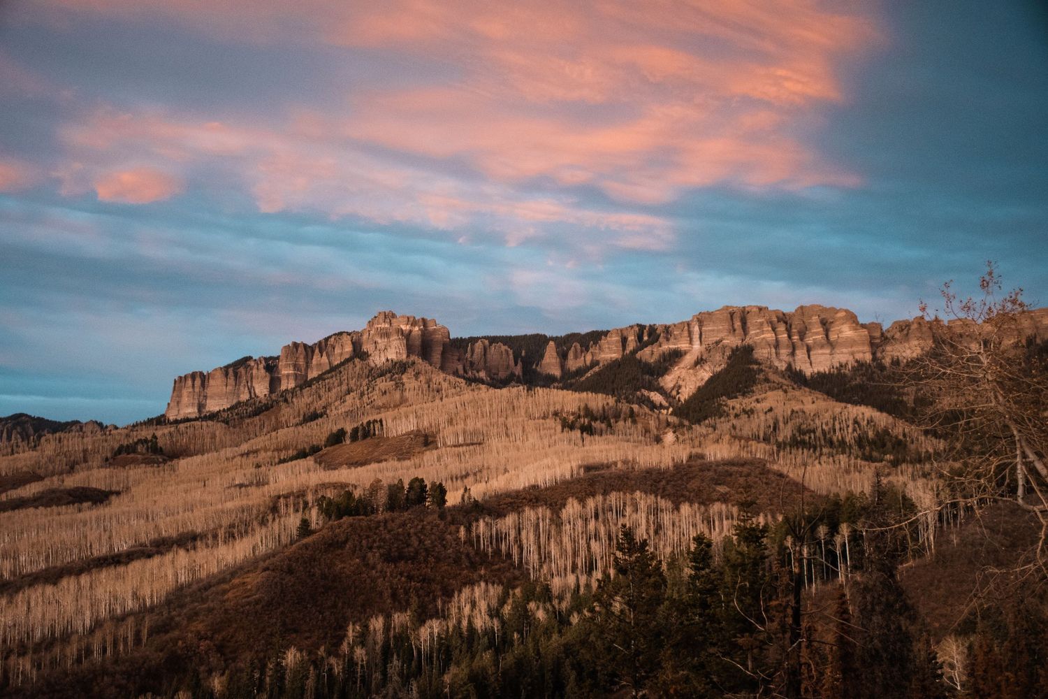 Rocky mountain cliffs illuminated by golden sunset light against a vibrant pink and blue cloudy sky.