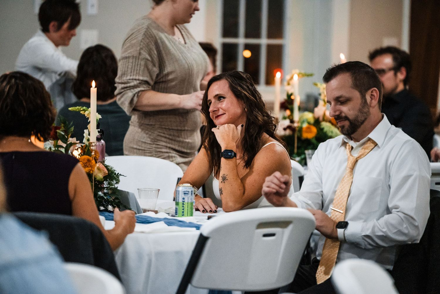 Wedding reception guests enjoying conversation and laughter at decorated tables.
