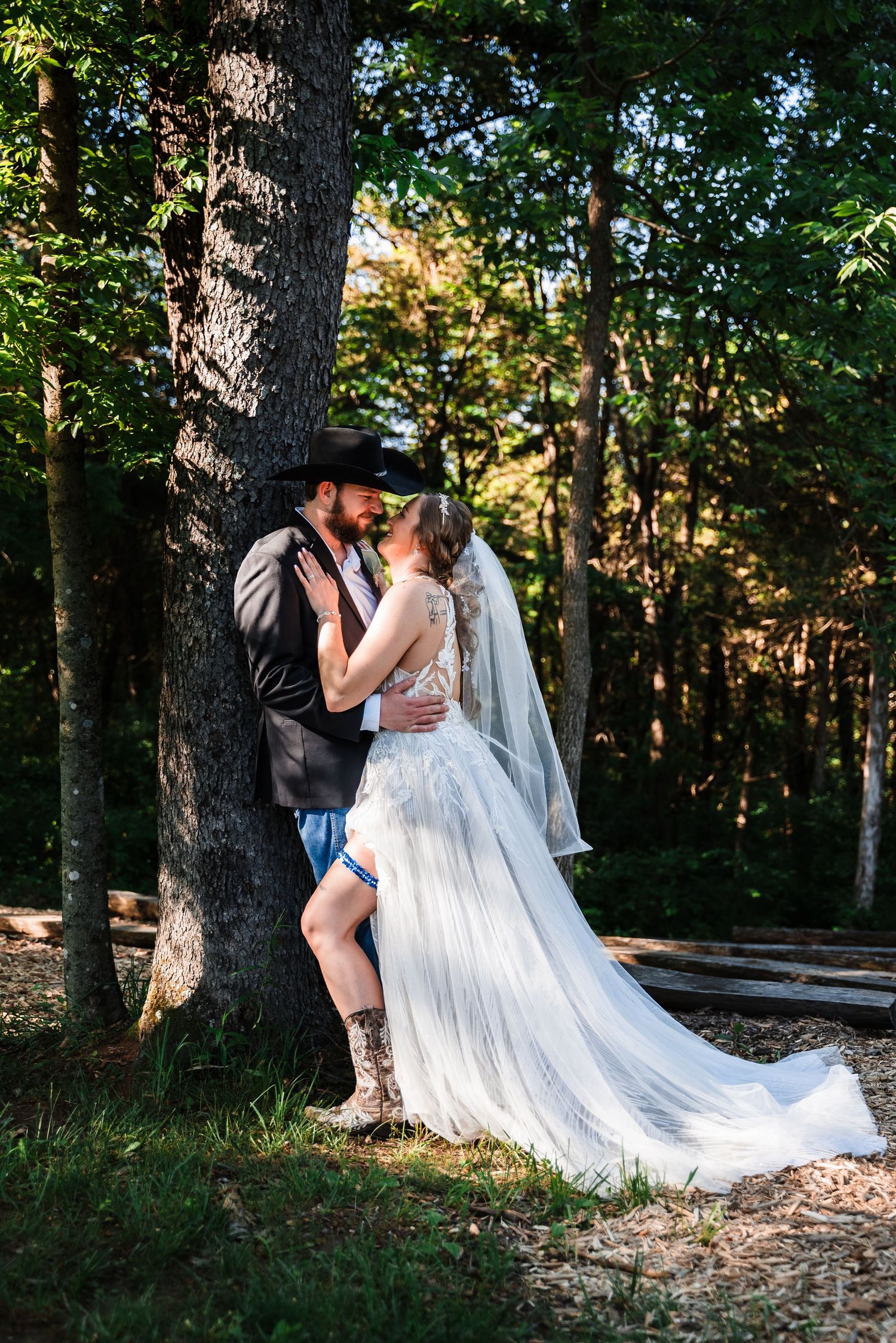 A romantic wedding photo in the woods showing a couple embracing against a tree with a flowing white dress.
