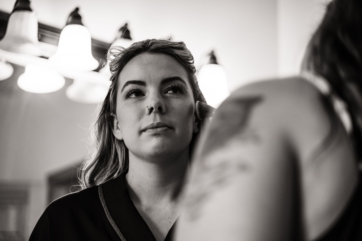 A black and white portrait in a bathroom with overhead lighting captures a close-up reflective moment.