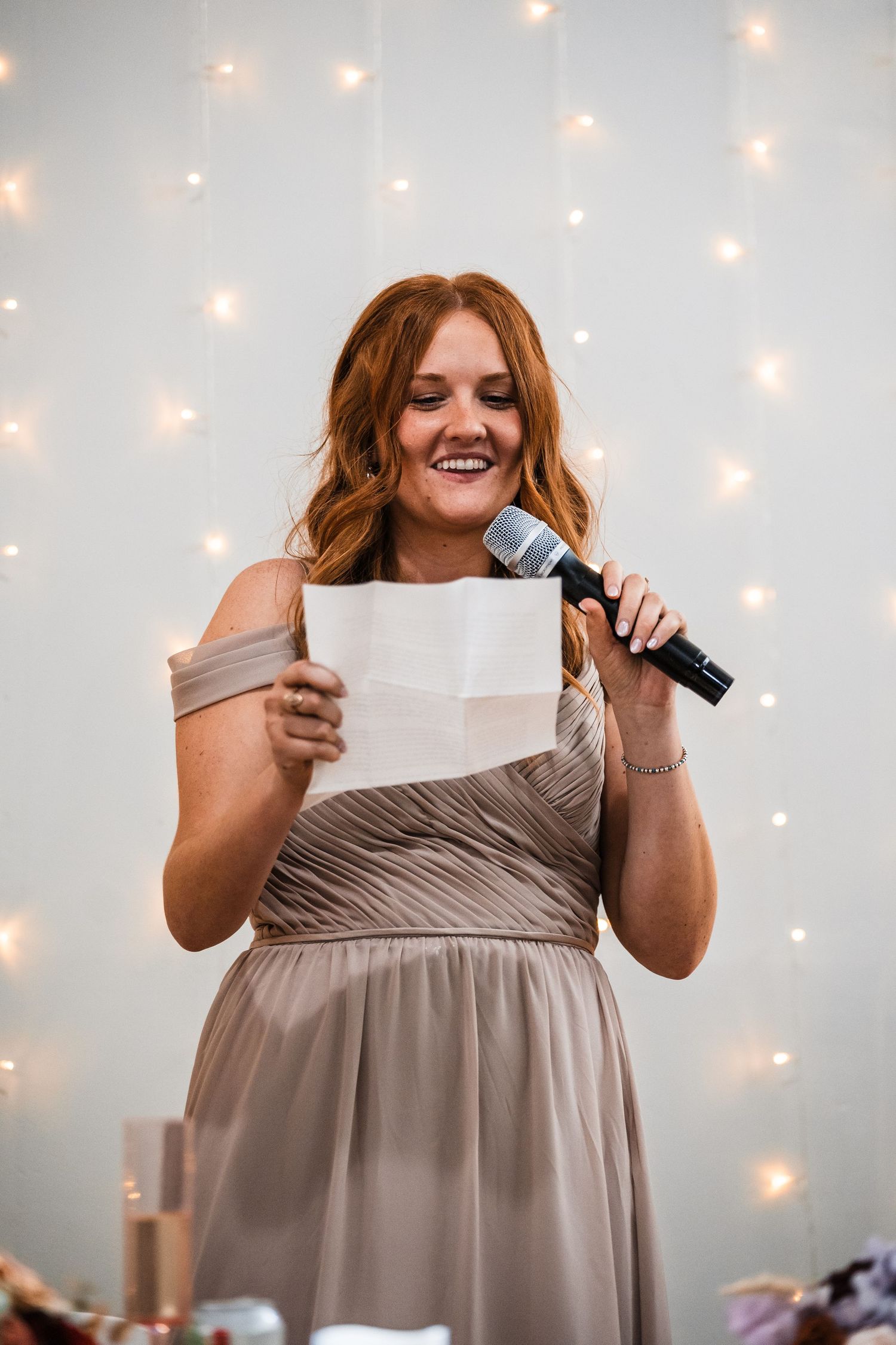 Person in a gray dress giving an emotional speech with string lights in the background.