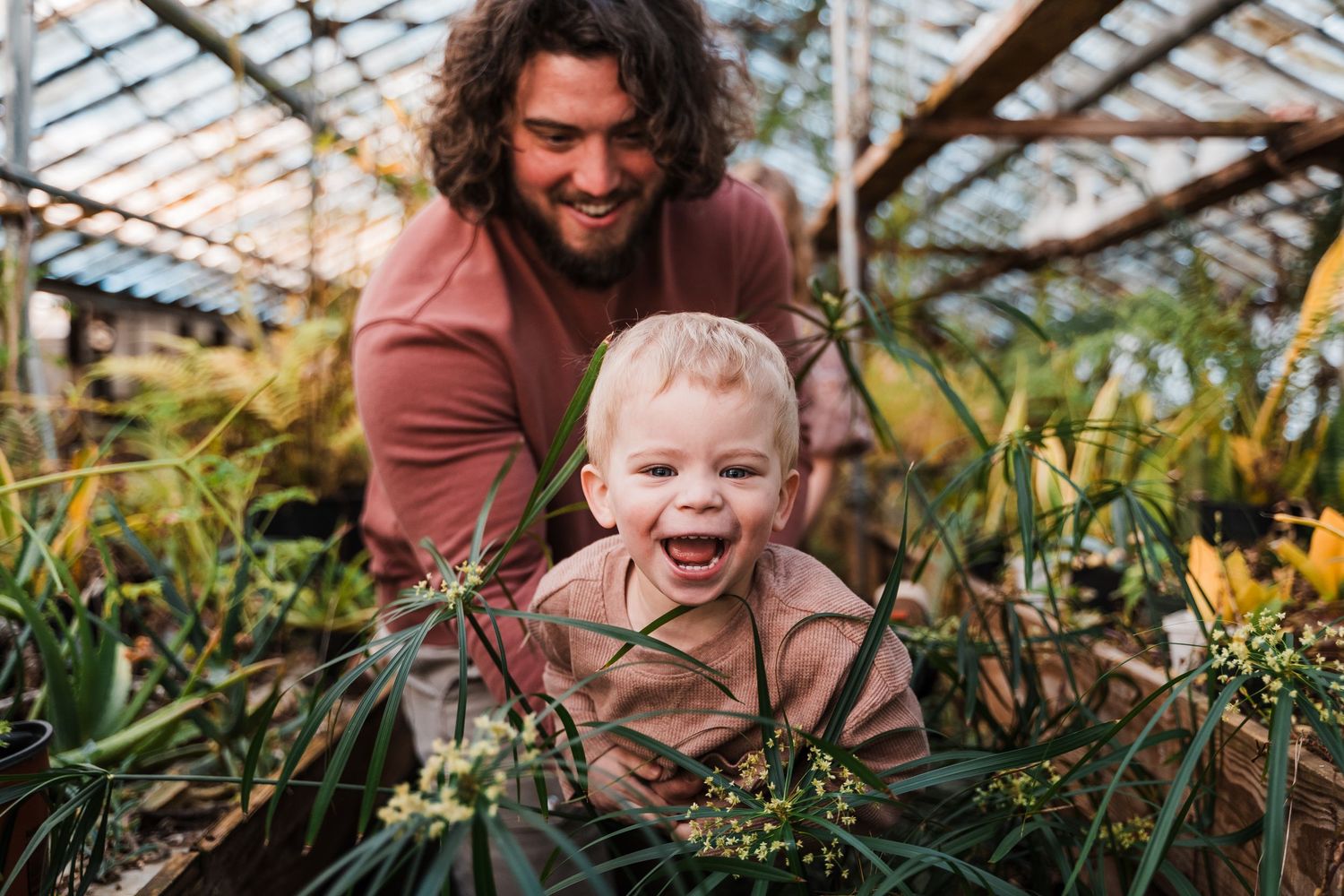 Happy people enjoying themselves in a lush greenhouse filled with tropical plants and natural sunlight.
