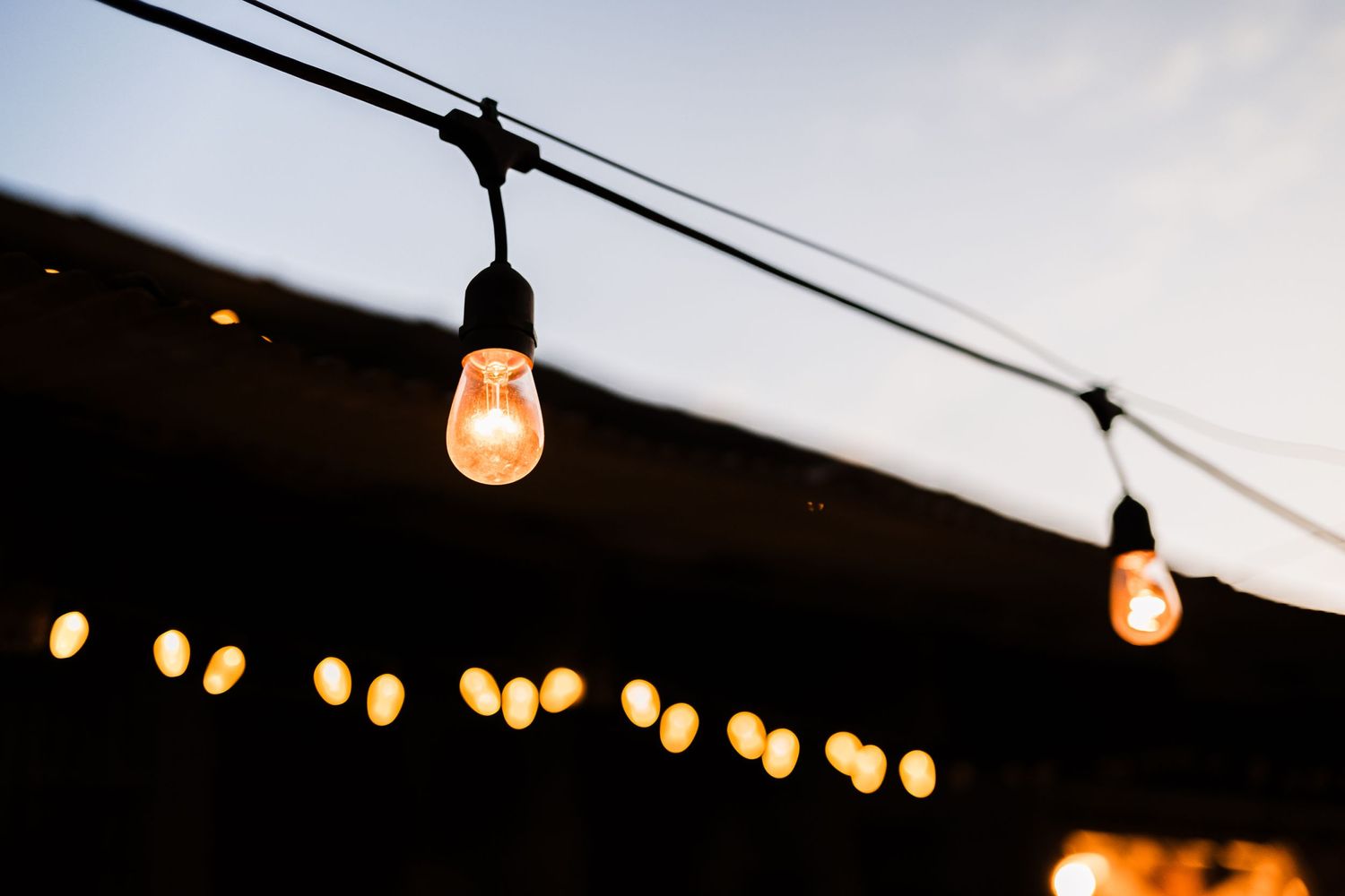 String lights create a warm ambiance with glowing bulbs against a dark evening sky.