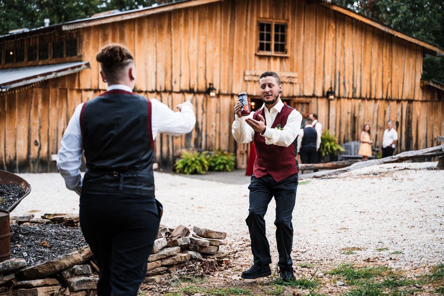 Two people in formal attire stand near a wooden barn in conversation.