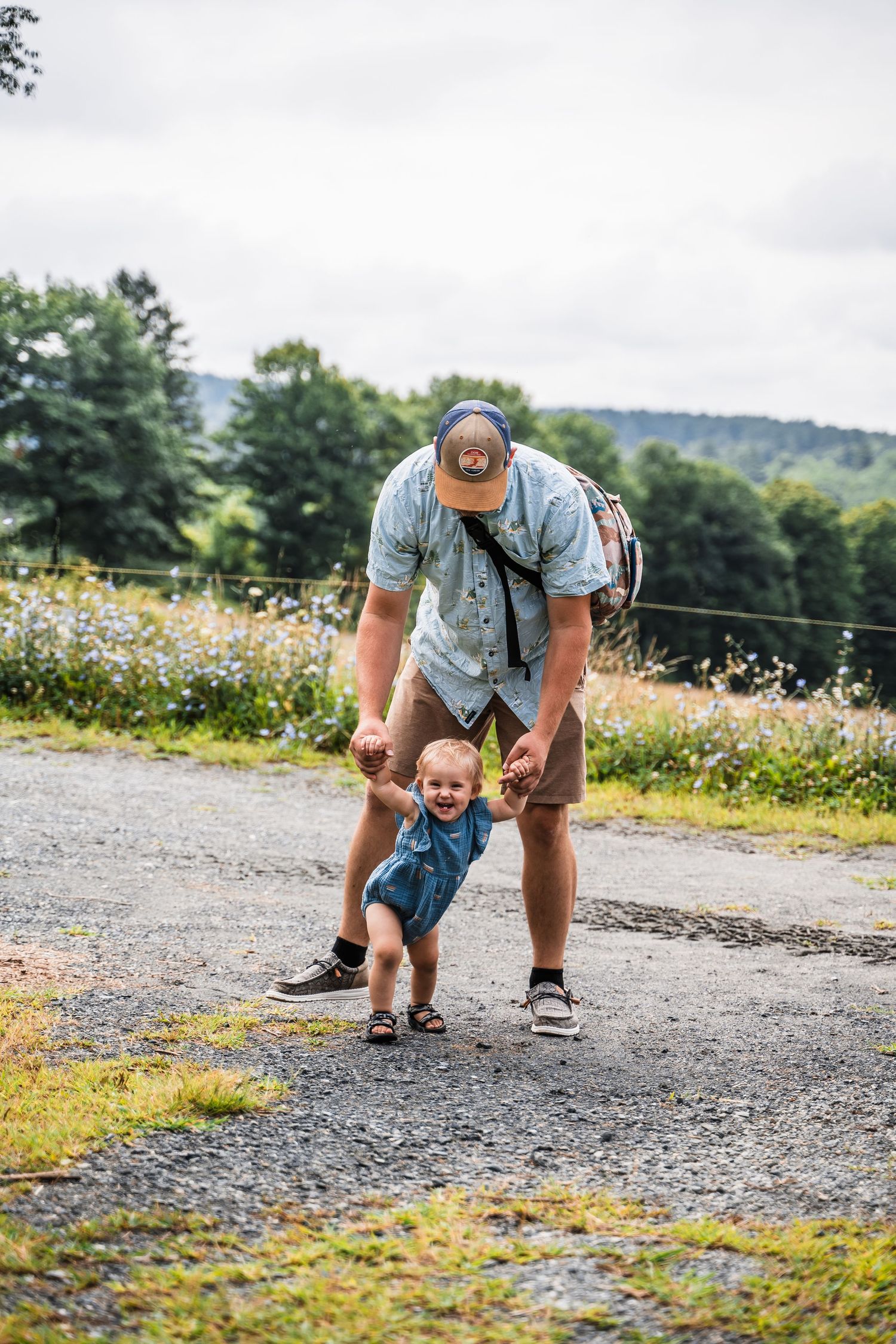 A playful moment on a country road with a toddler in denim being supported while walking outdoors.