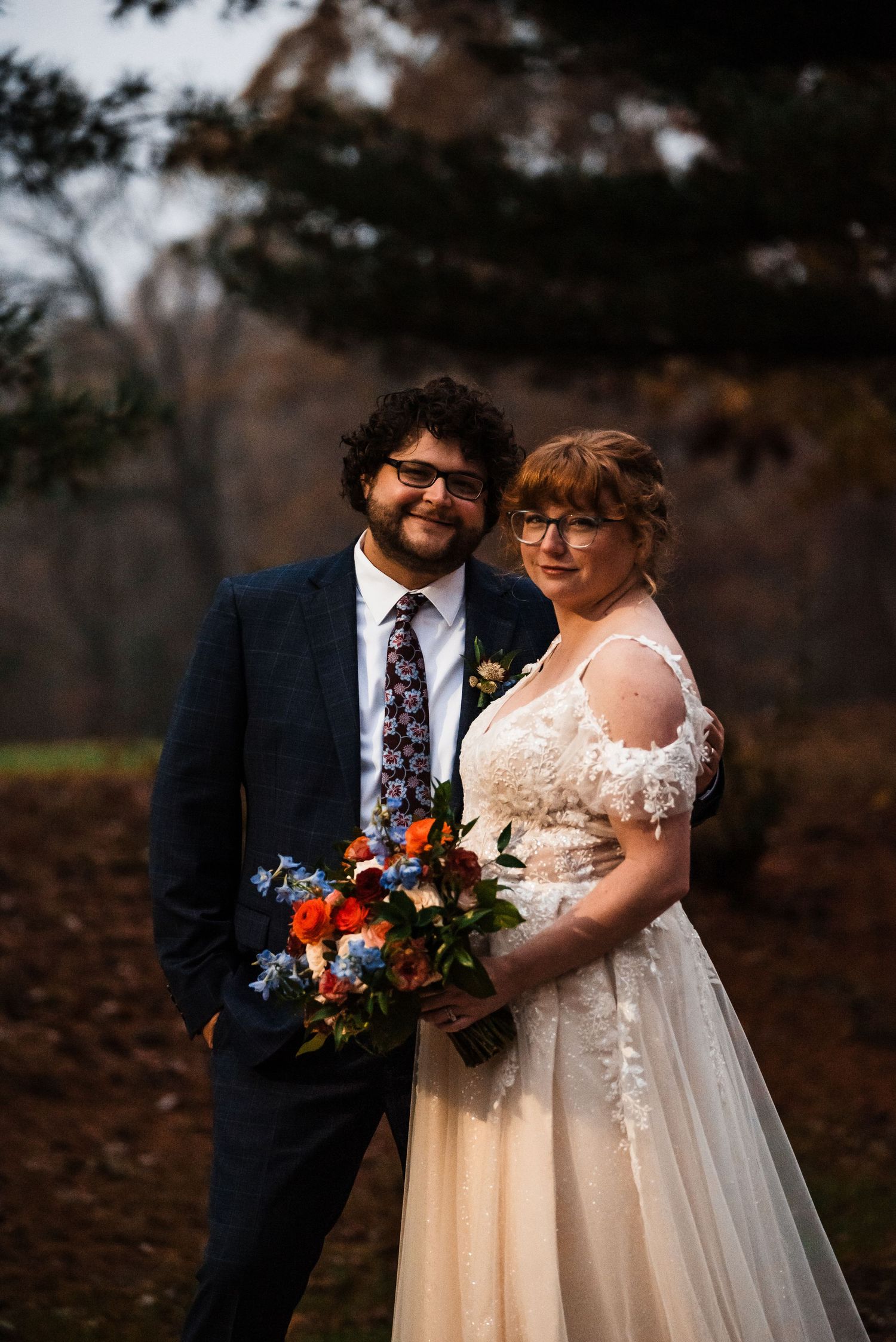 Wedding portrait in a dark forest setting with vibrant fall bouquet.