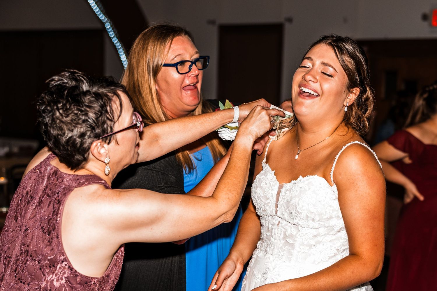 Wedding celebration with guests dancing and embracing joyfully during an indoor evening reception.