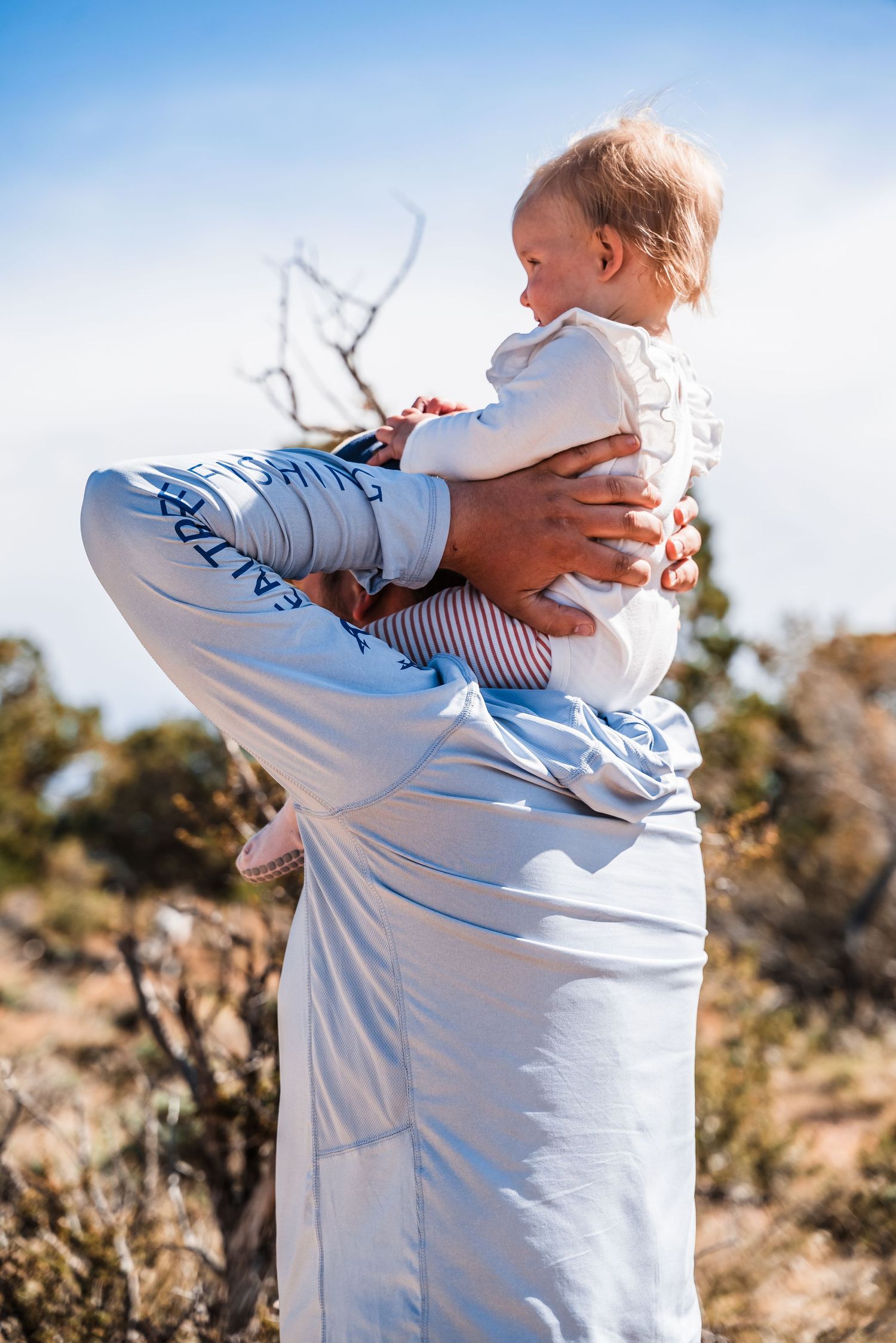 A tender moment showing a child being held up against a bright blue desert sky background.