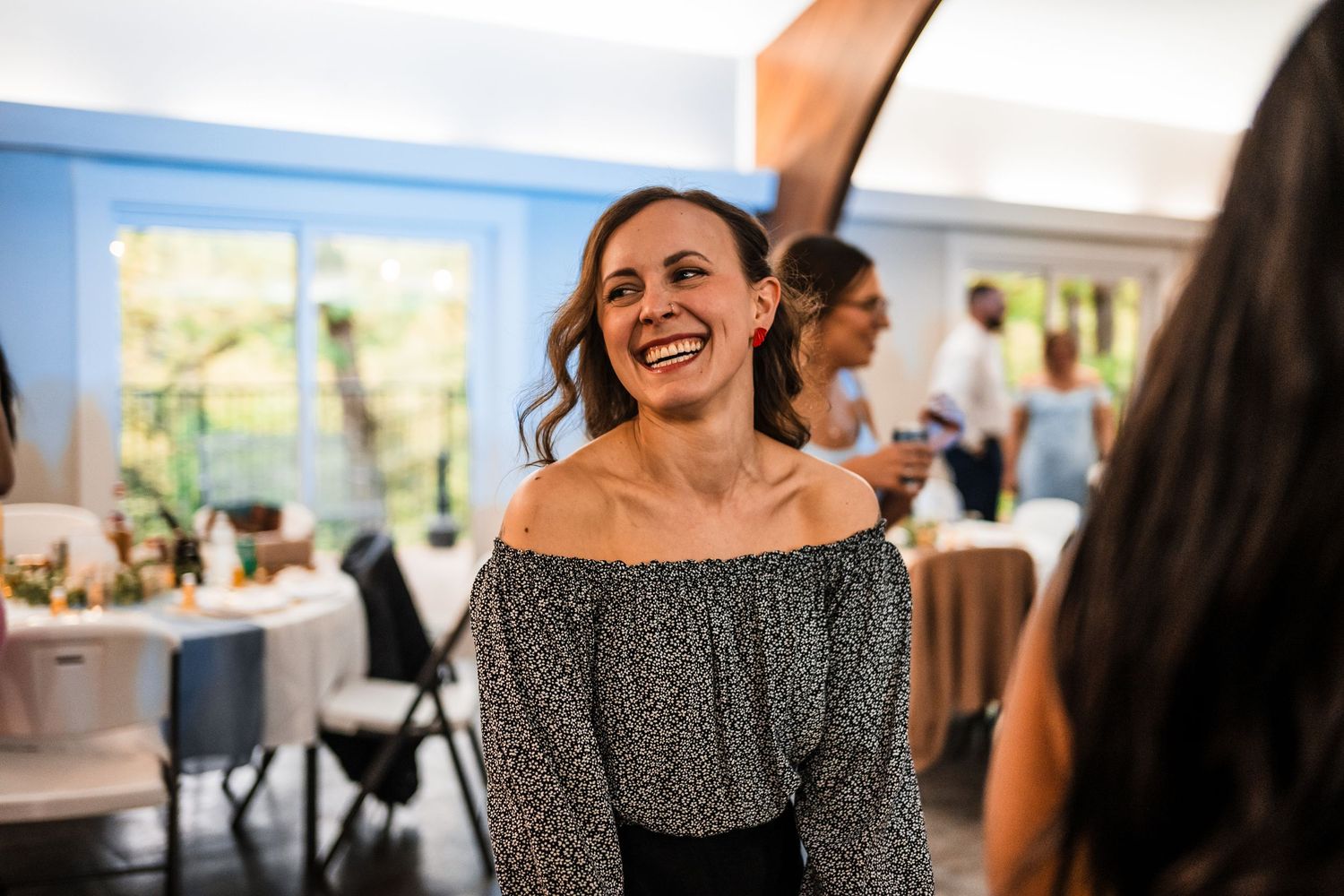 Woman in off-shoulder polka dot top smiling at a wedding reception.