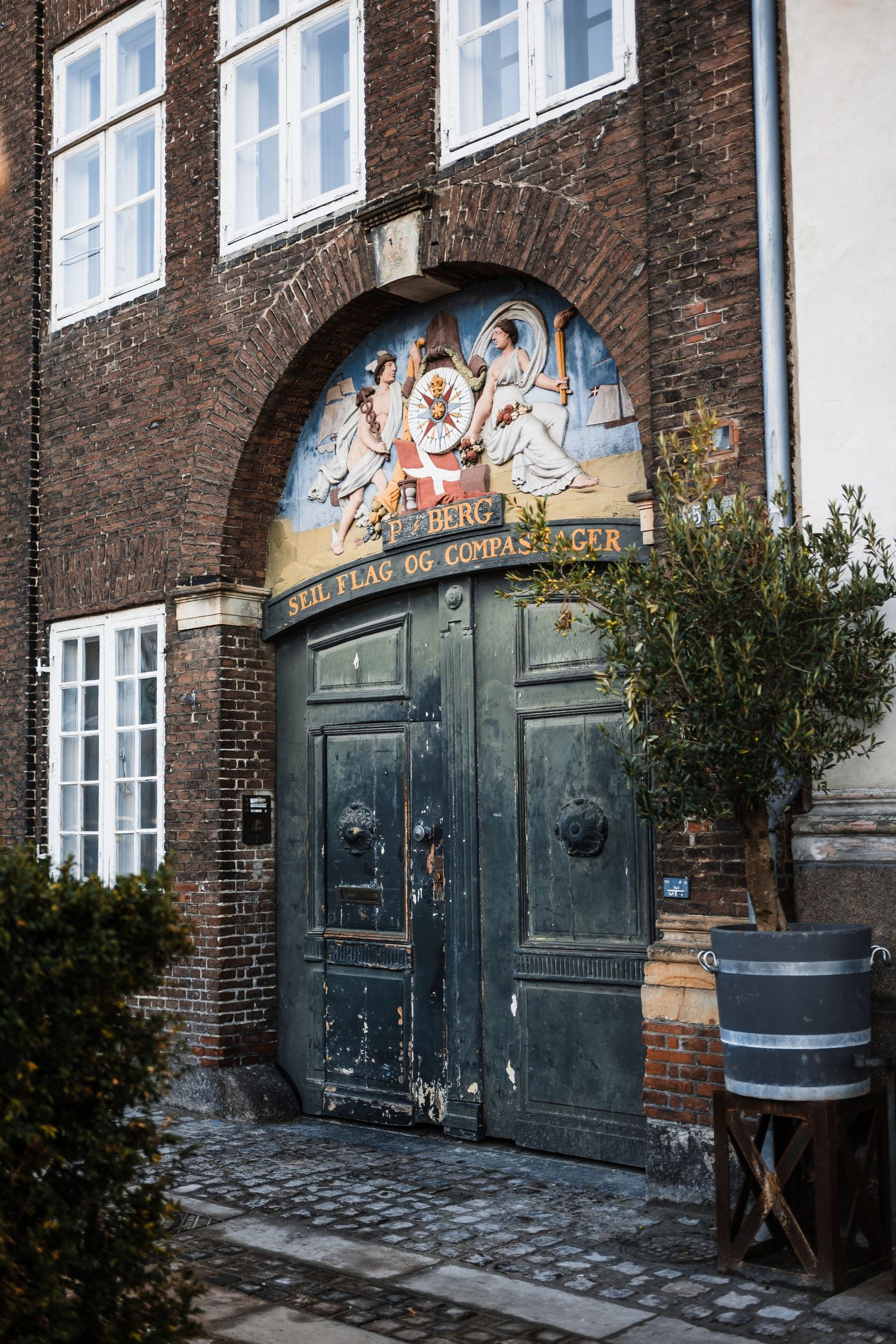 Rustic green double doors with graffiti art on a brick building facade with windows above and cobblestones below.
