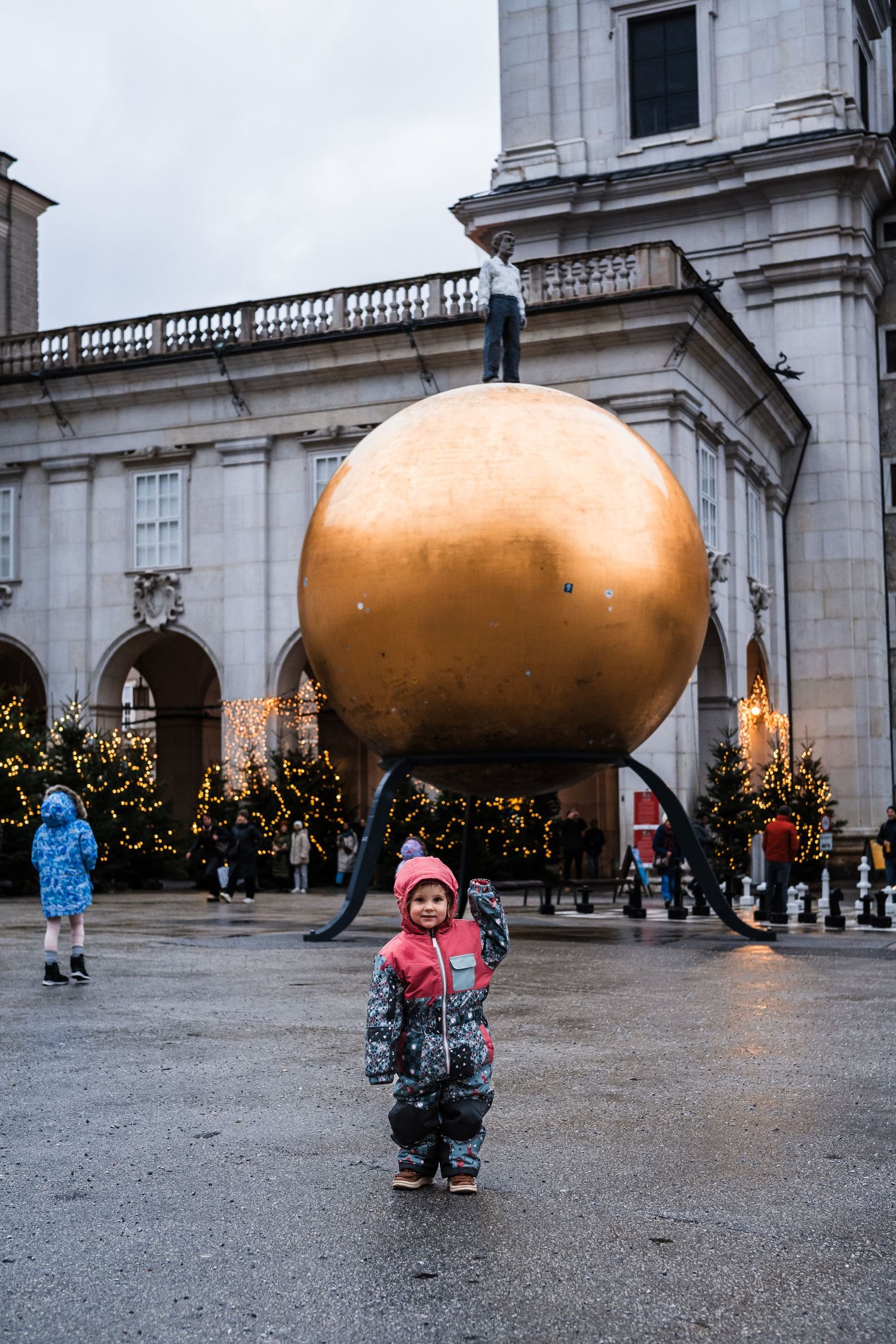 Large golden spherical art installations outside a classical building with visitors exploring.