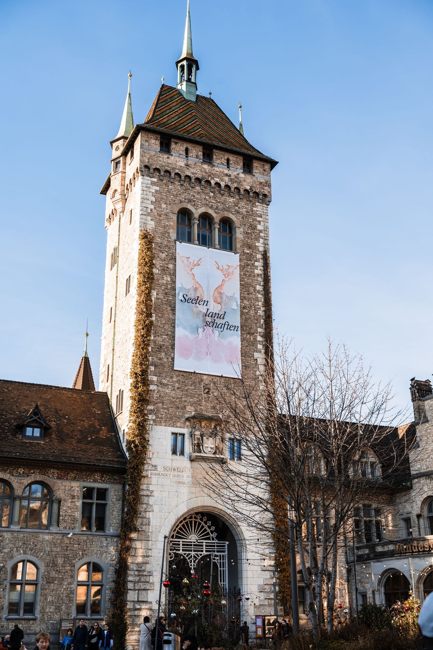 Historic stone tower with spire and banner stands against blue sky in Swiss architectural style.
