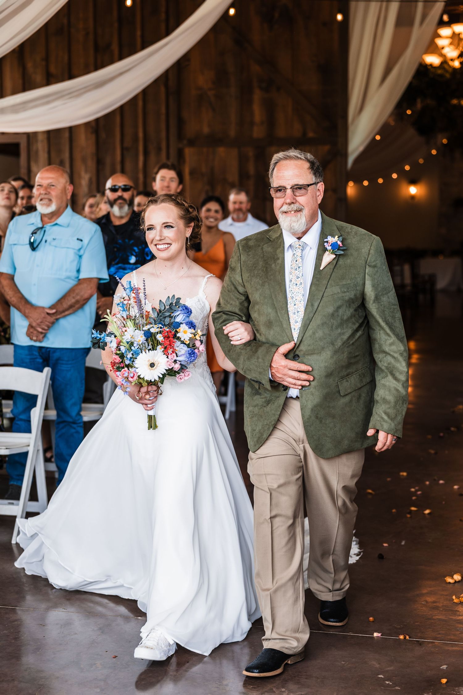 Bride walks down the aisle with her father in a rustic barn wedding venue.
