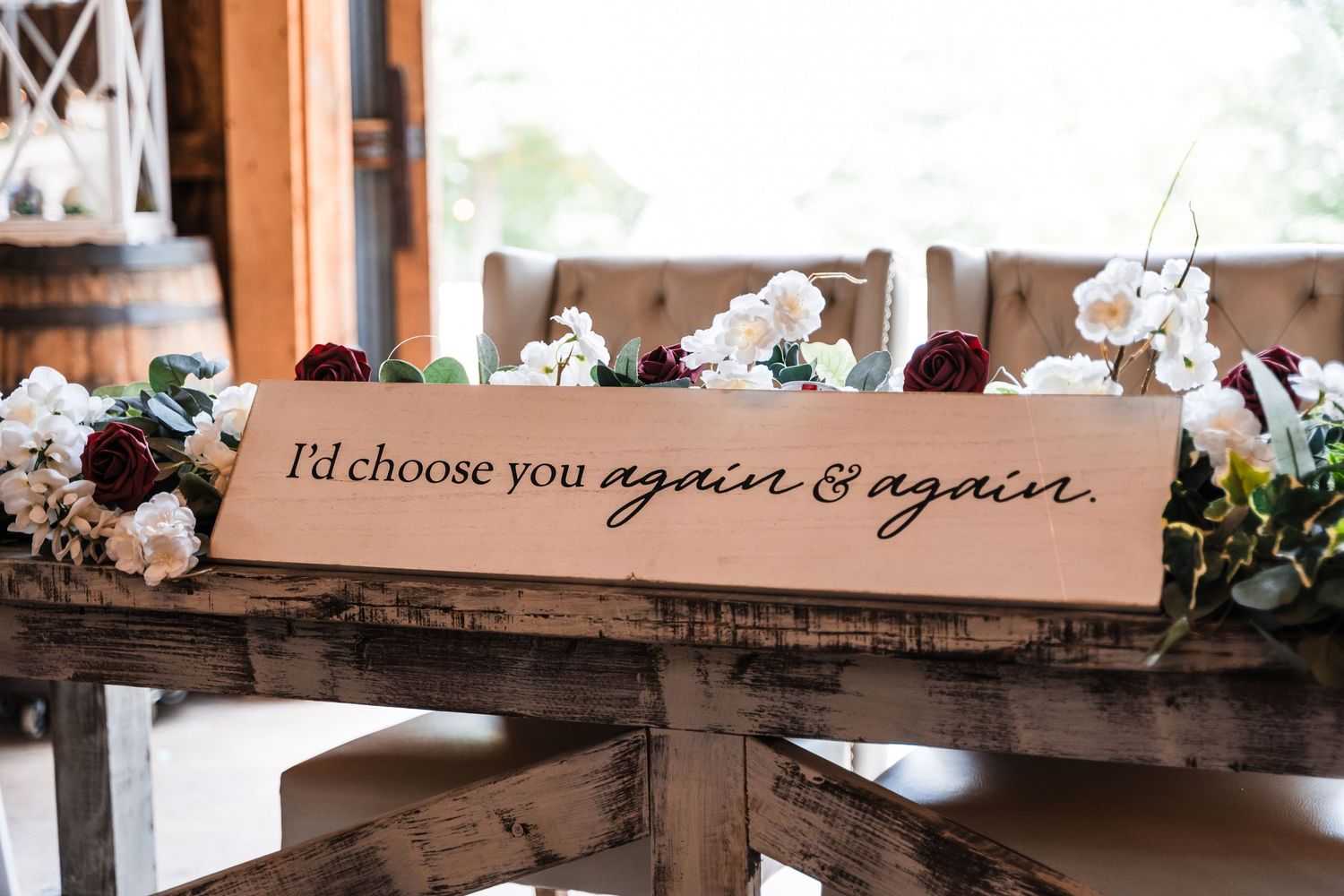 Wooden sign with romantic text displayed on rustic table with floral decorations.