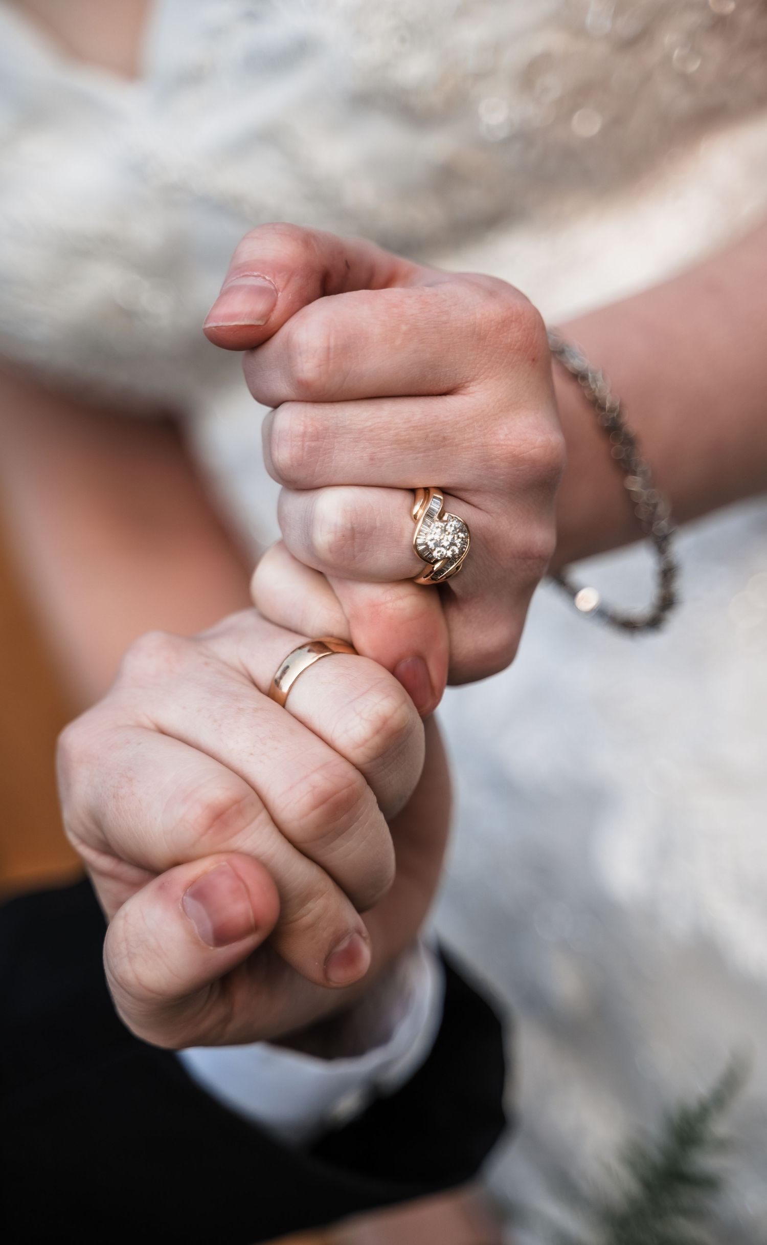 Close-up of clasped hands showing wedding rings and delicate lace dress details.