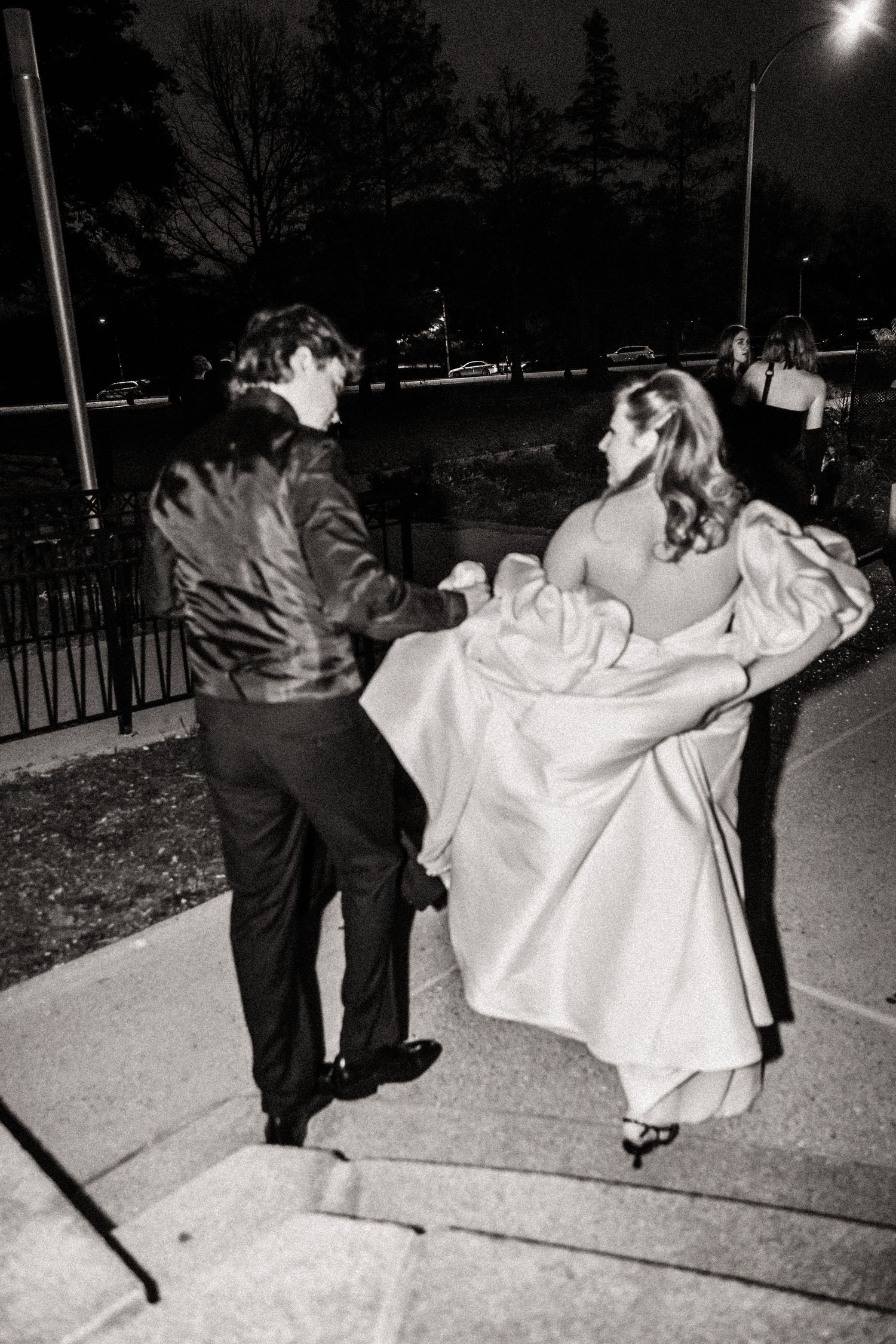 Black and white photo of couple dancing together on a nighttime sidewalk.