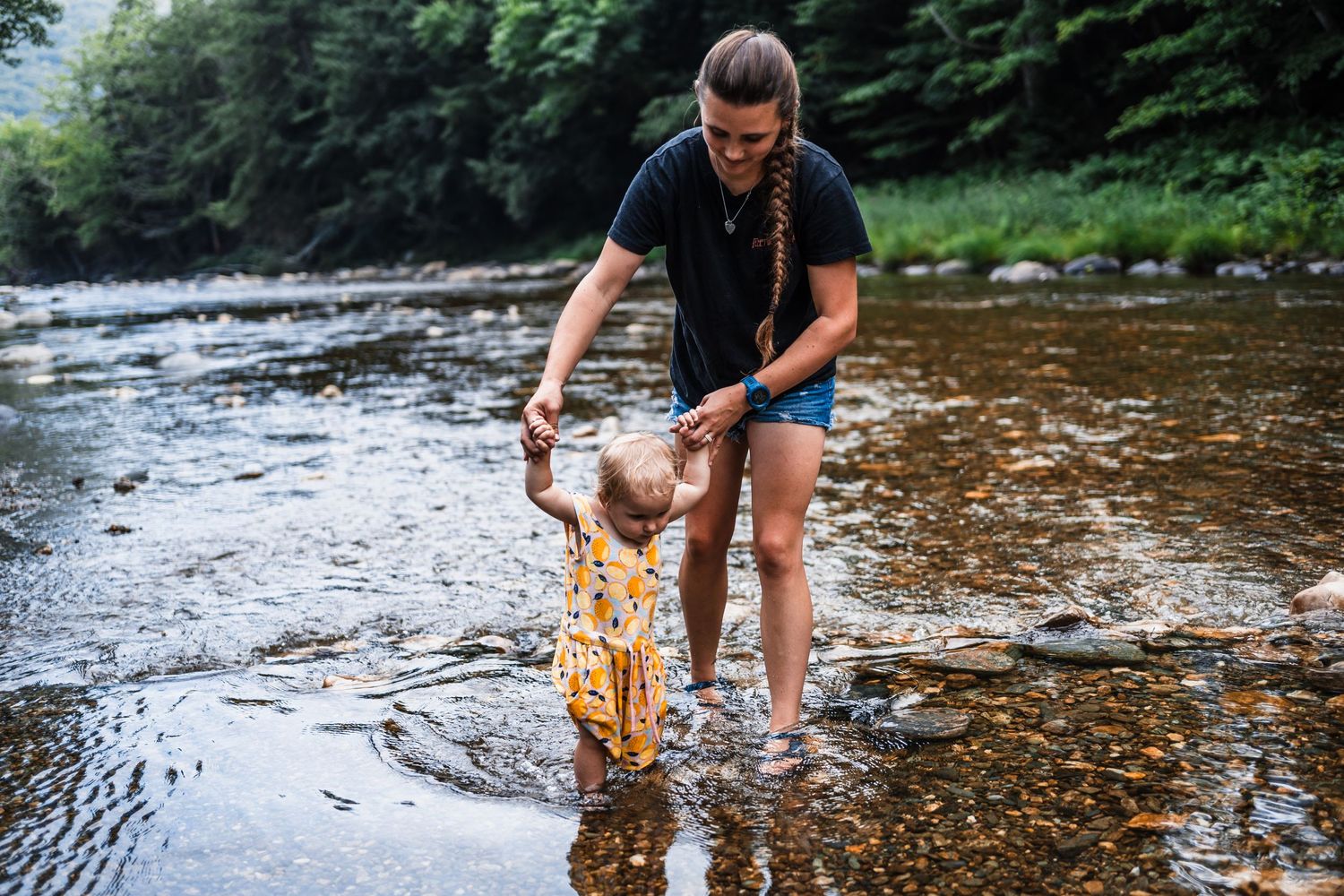 Person testing water quality by collecting a sample from a flowing river on a summer day in a wooded area.
