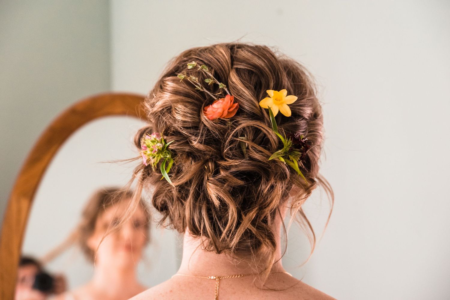 An elegant updo hairstyle adorned with small colorful flowers for a wedding day.