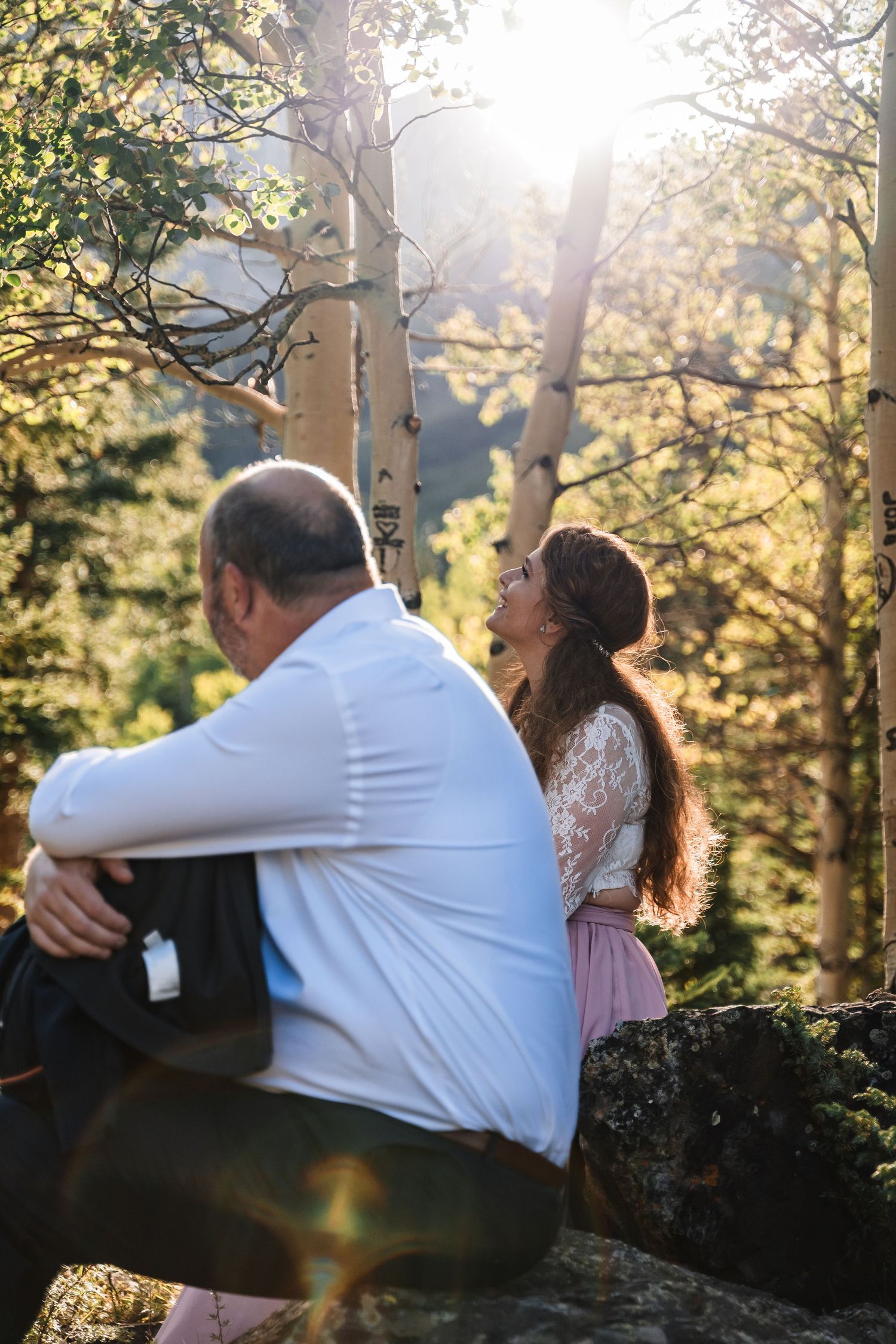A sweet moment shared between two people in a sunlit forest setting.