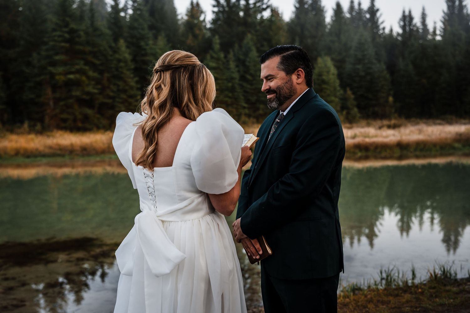 Newlyweds share an intimate moment while reading vows against a forest backdrop.