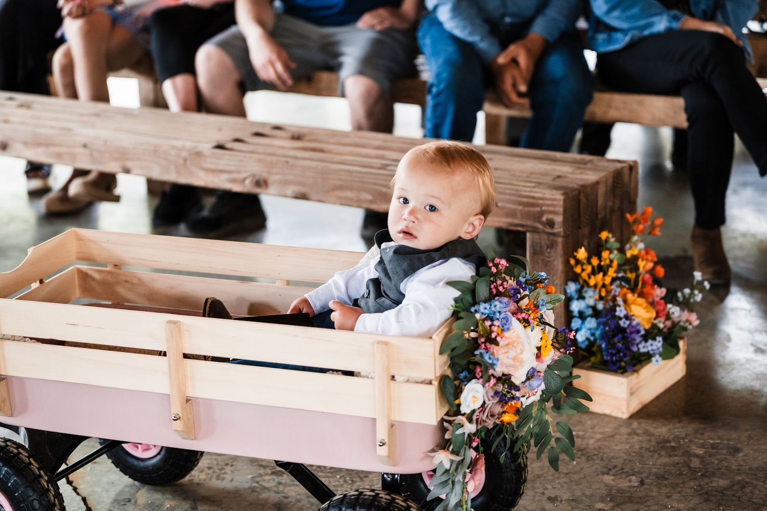 A small child rides in a decorated wooden wagon with colorful floral arrangements.