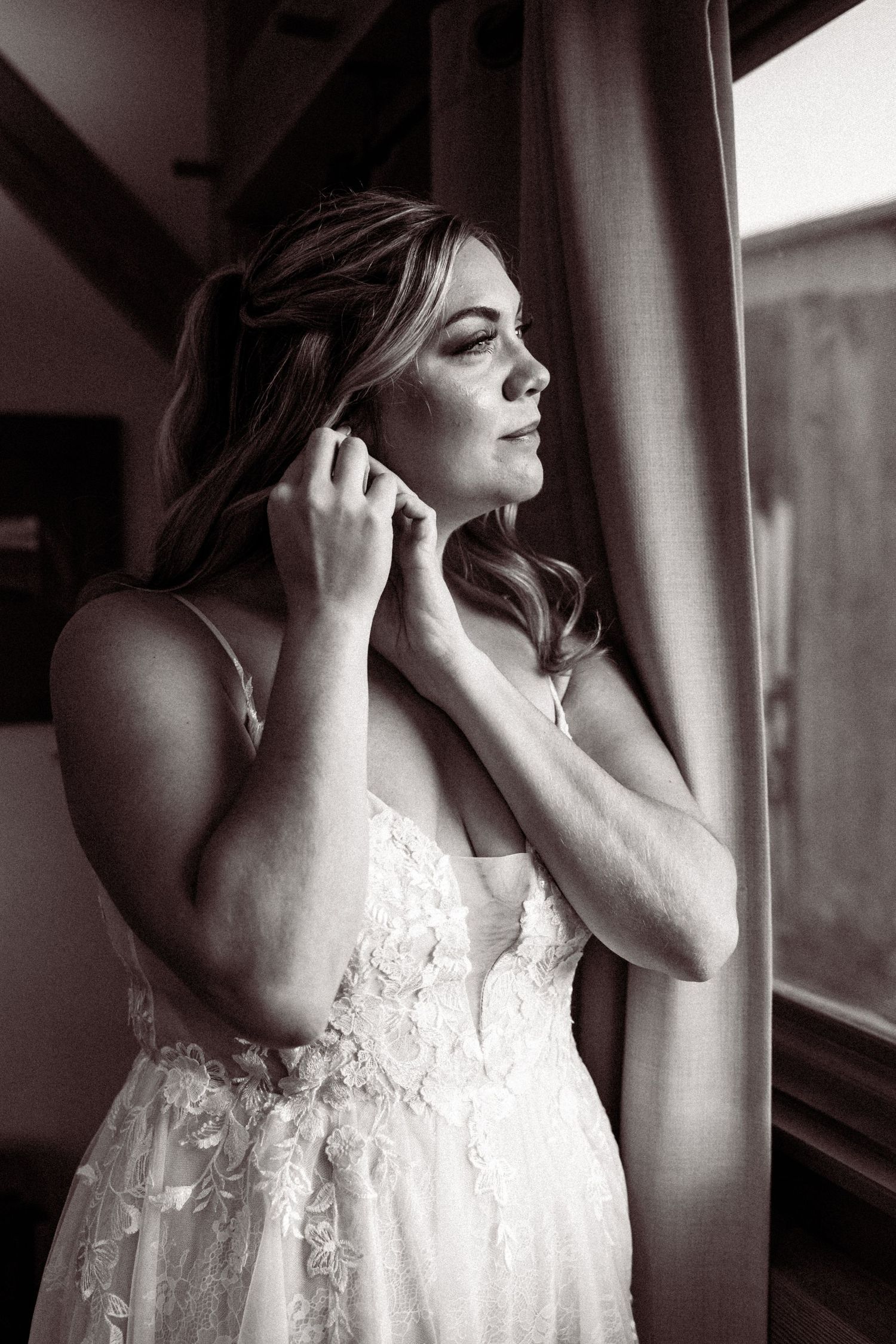 Artistic black and white series of a bride in a lace dress getting ready by a window.