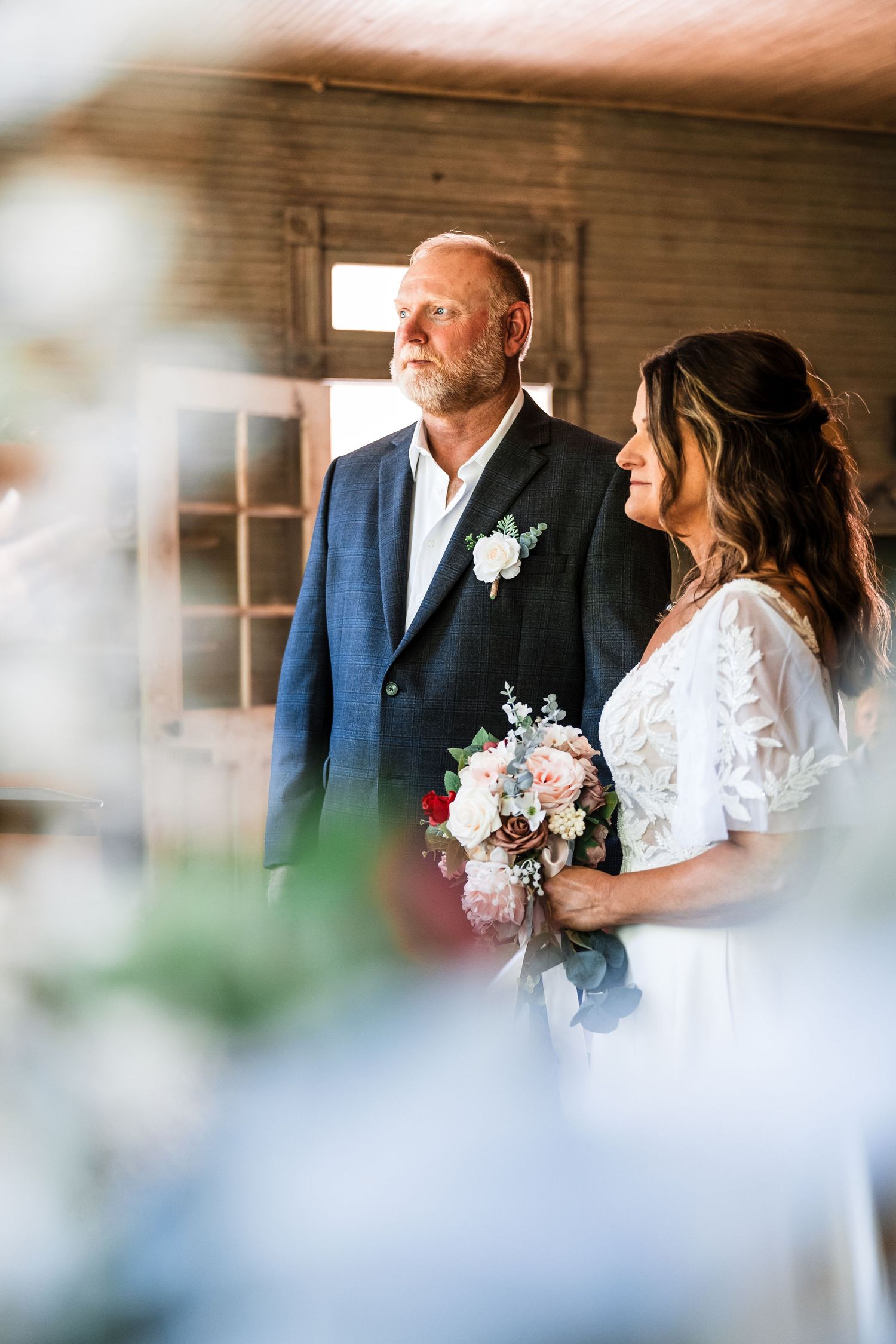 Romantic wedding photography through window glass showing couple in rustic barn setting.